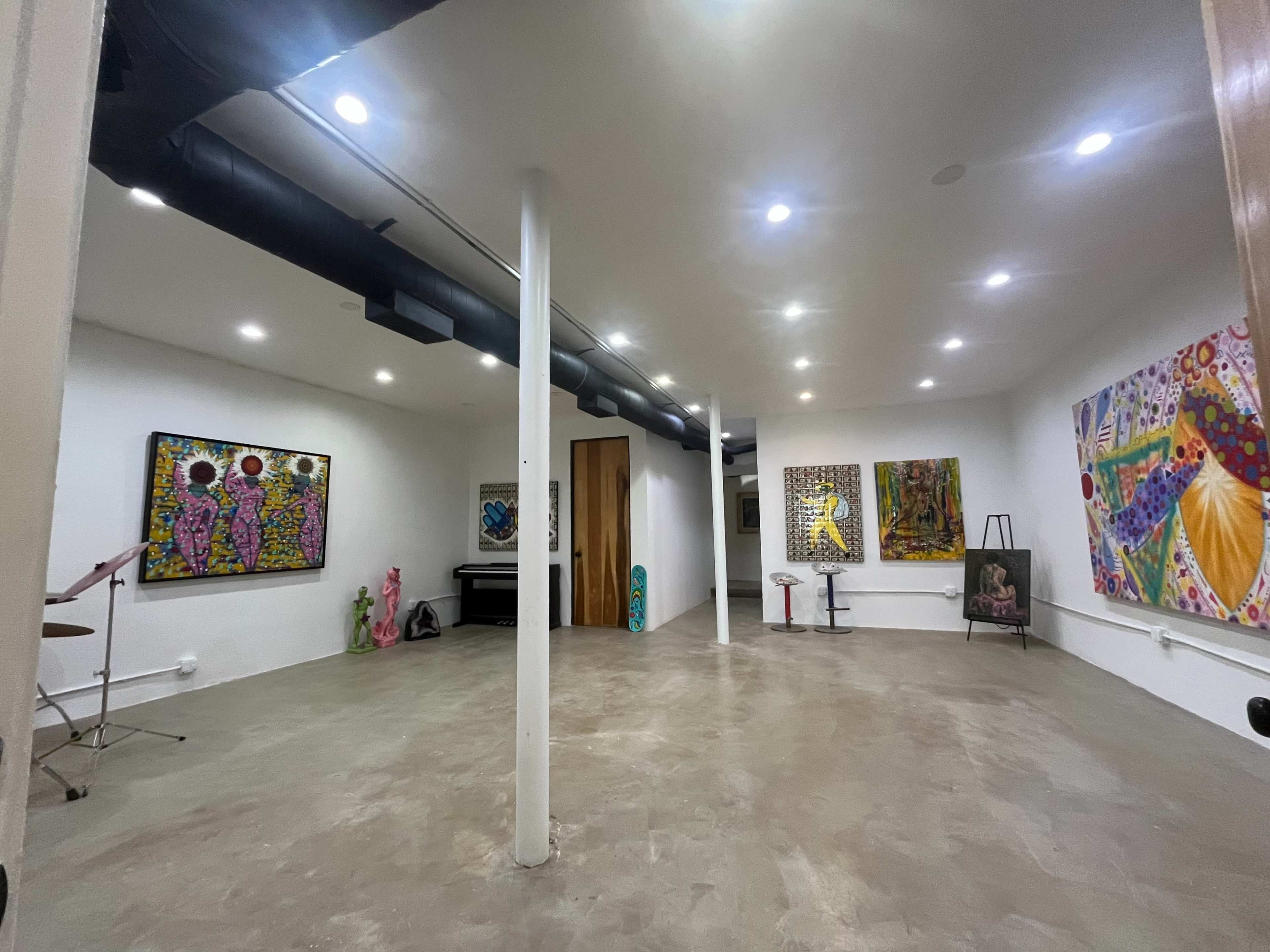 The image shows a spacious art studio or gallery with several colorful paintings on the walls, a keyboard, and various art supplies scattered around the room.