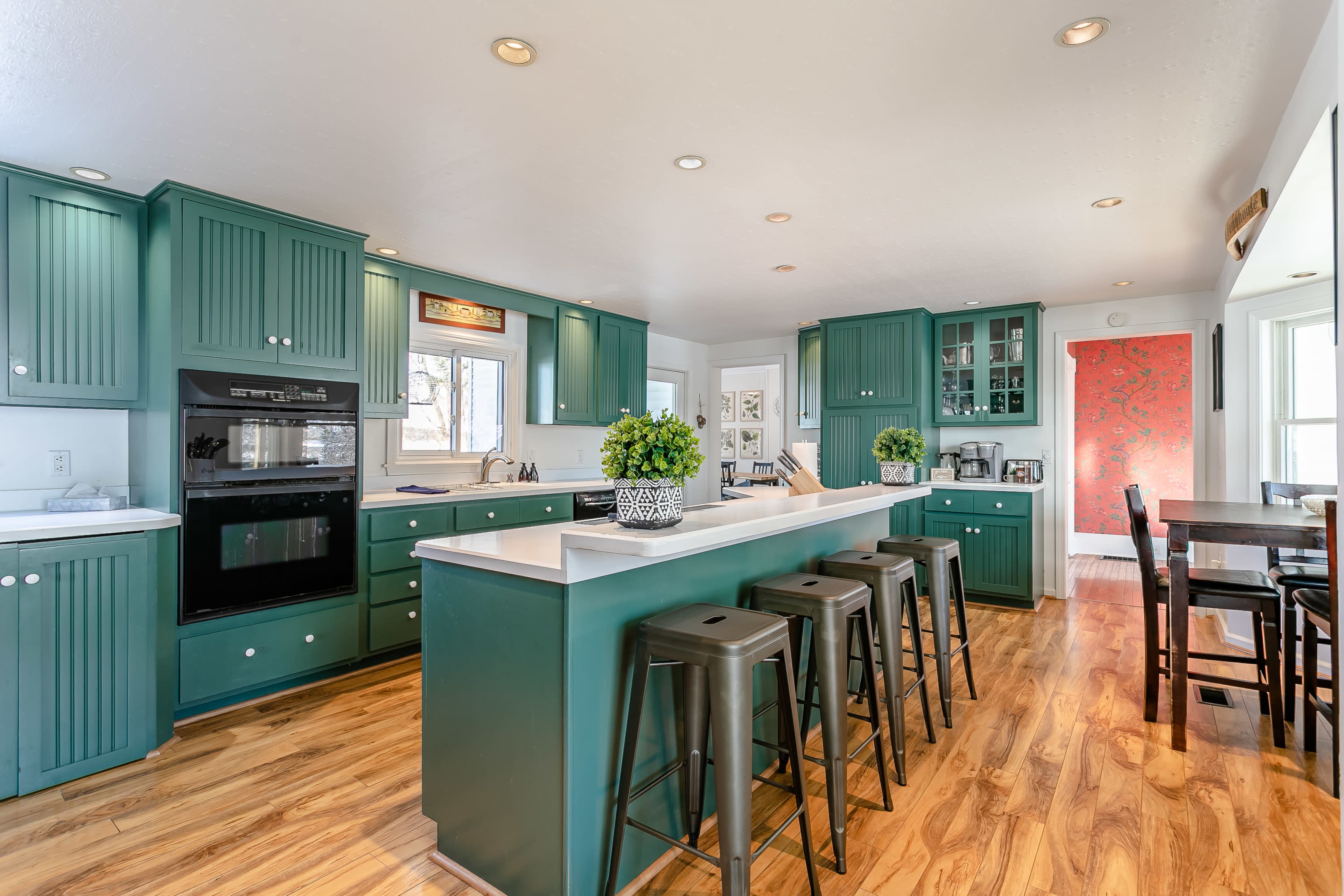 A modern kitchen with green cabinets, a central island with bar seating, and light-colored countertops.