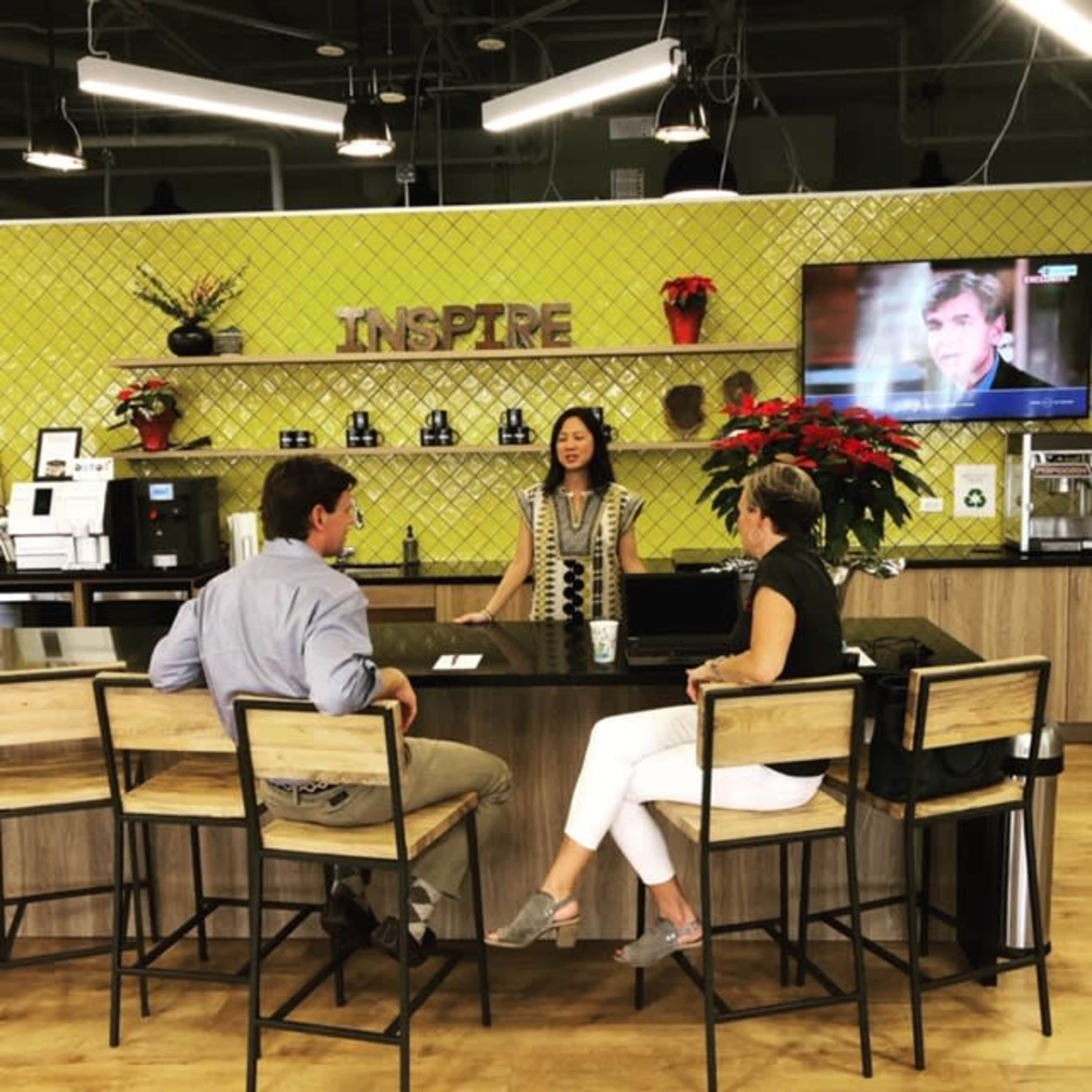 A woman stands behind a counter in a modern cafe while two seated people engage in conversation.