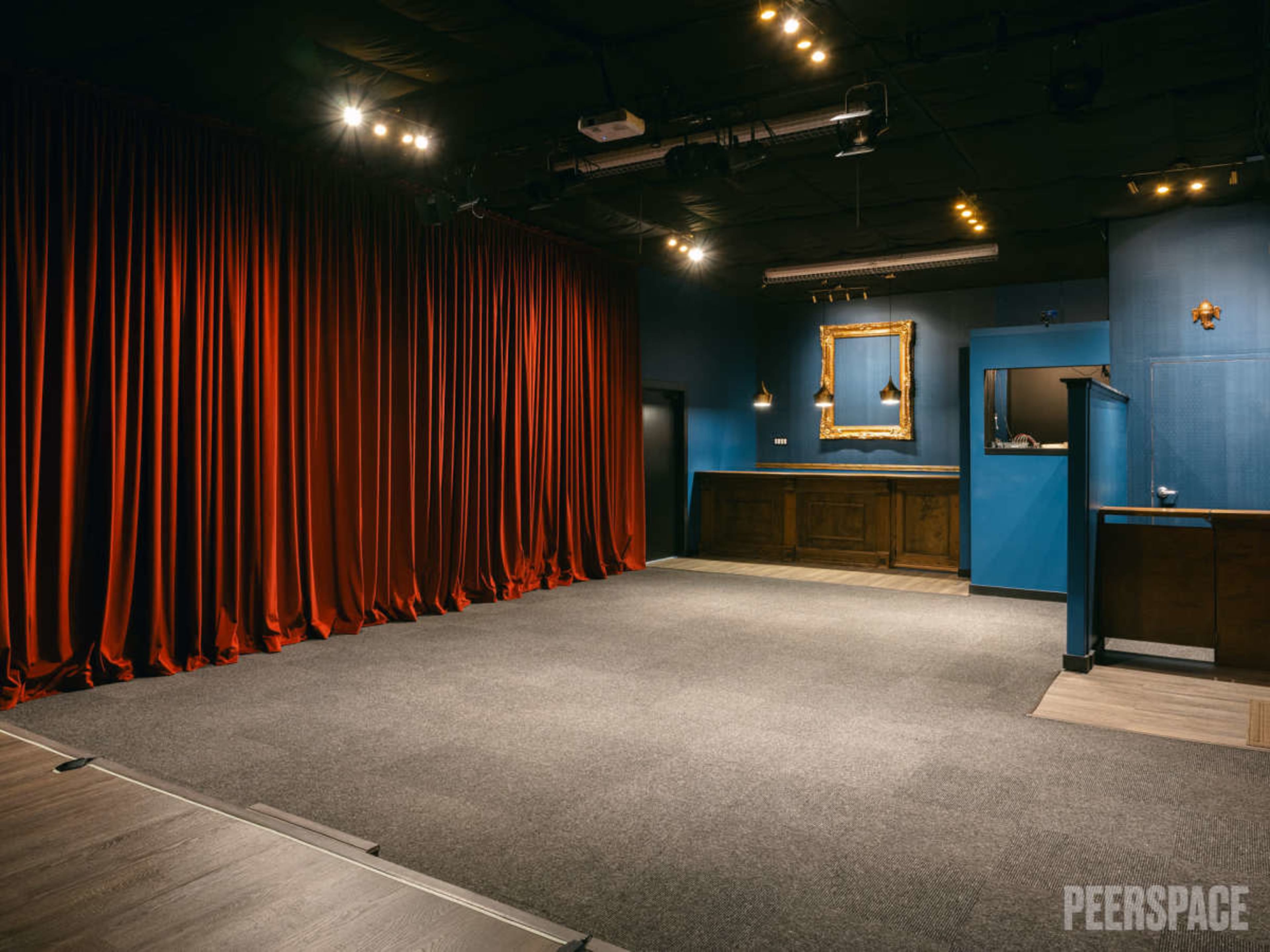 A performance space featuring a red curtain, a gray carpeted floor, and a blue-walled area with a wooden reception counter and a framed mirror.