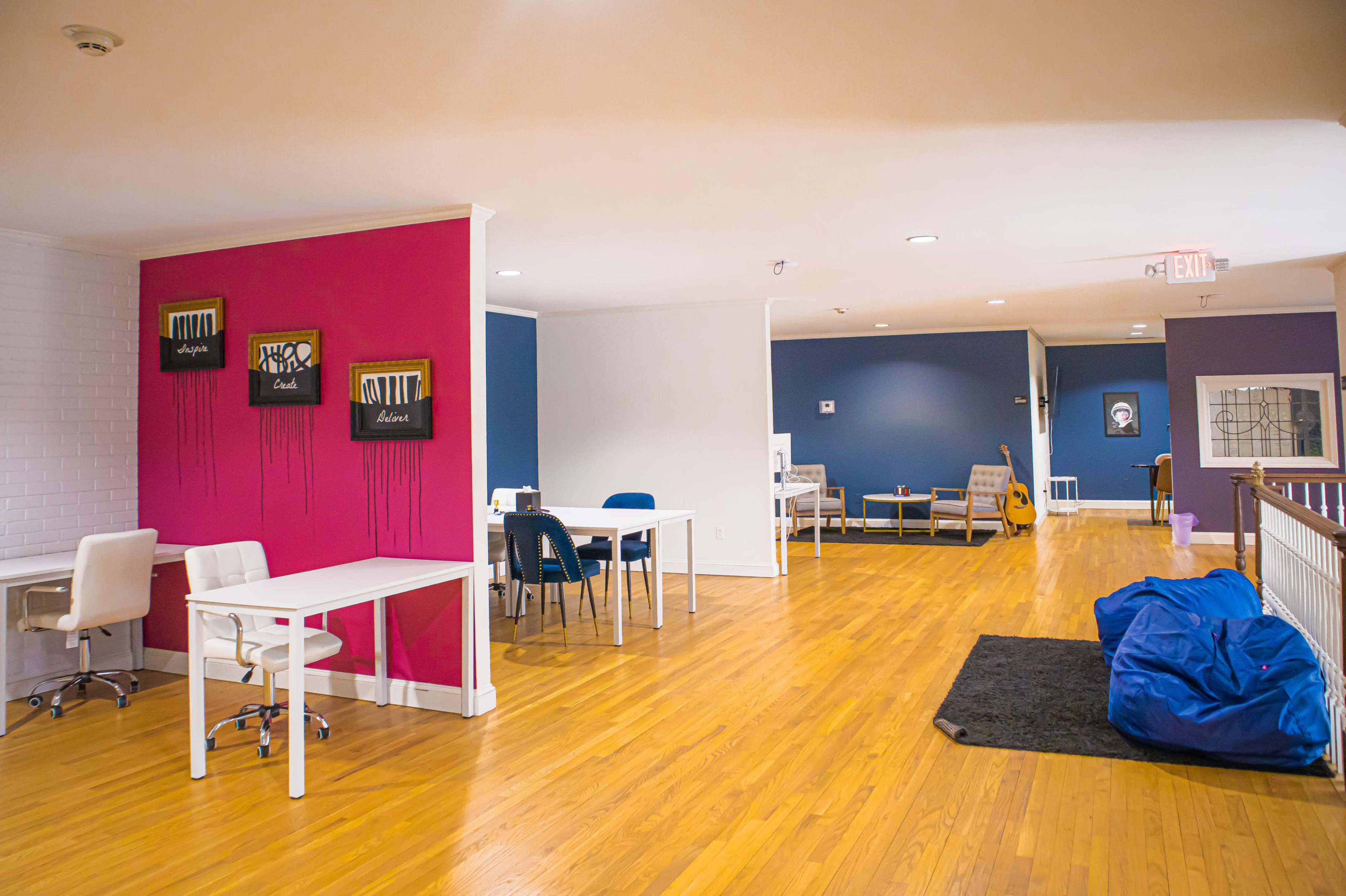 A modern interior space featuring wooden flooring, colorful accent walls, multiple workstations, and a lounge area with furniture.