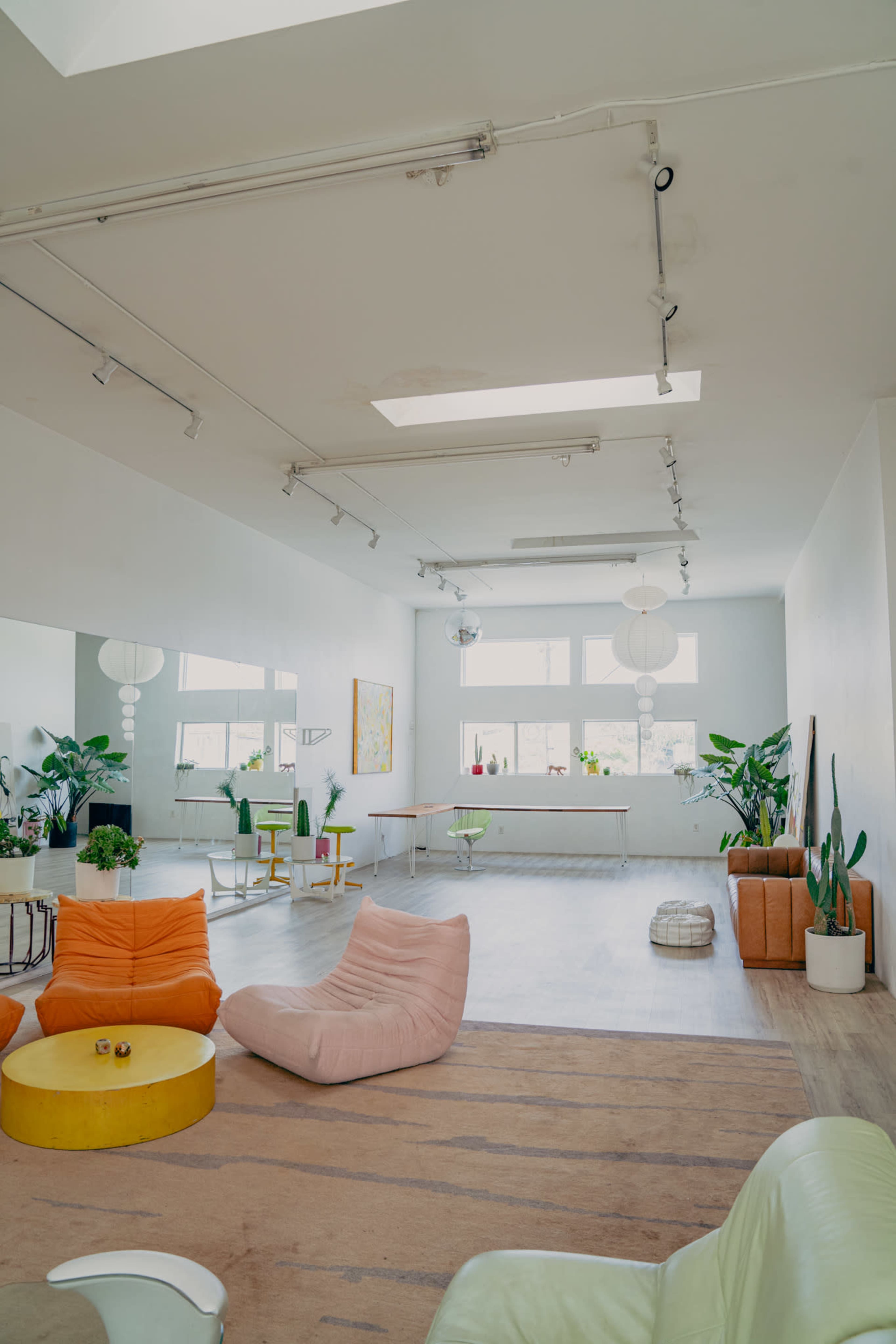 The image shows a spacious, well-lit room with a mix of seating options, plants, and decorative elements.