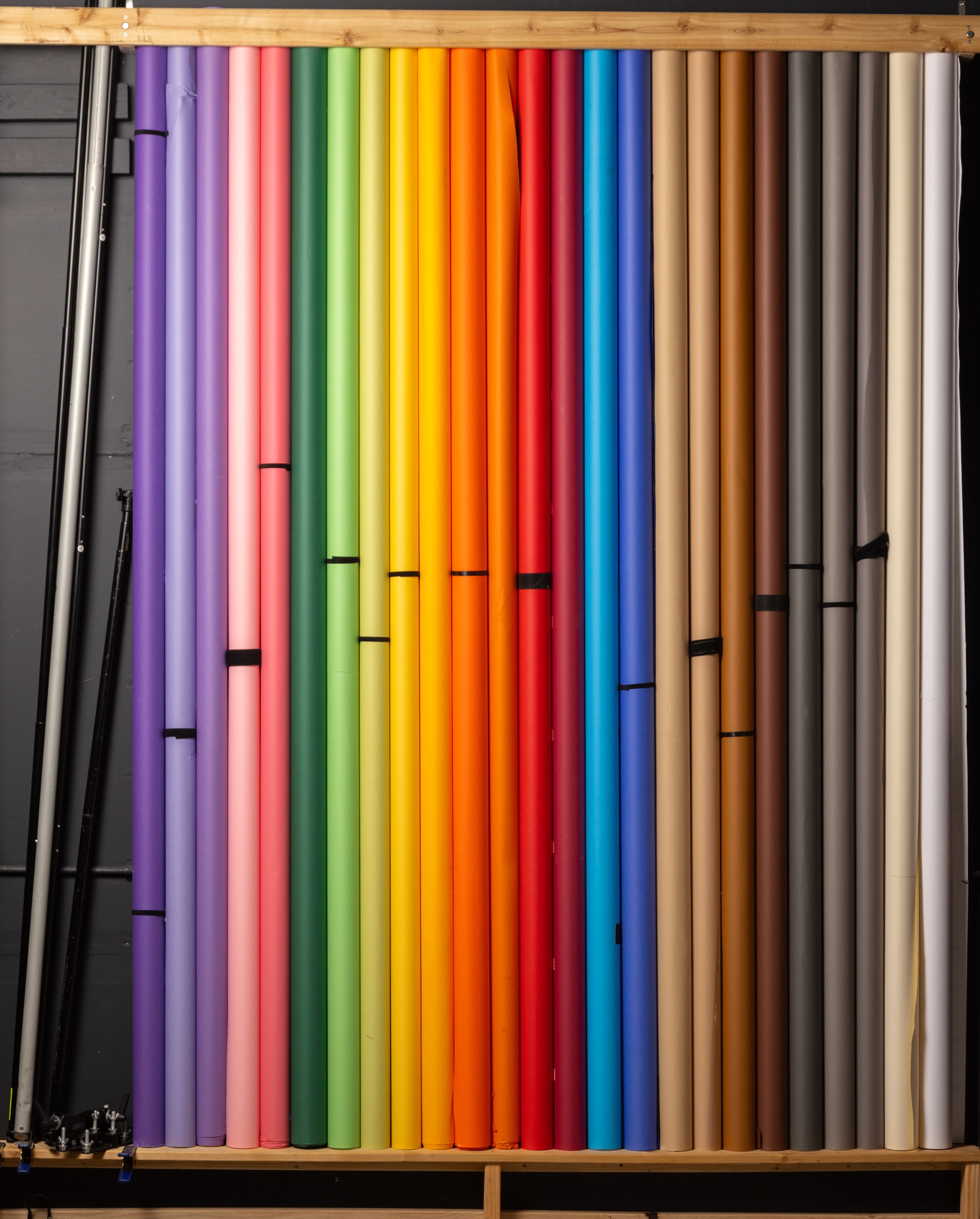 The image shows a vertical arrangement of various colored backdrop rolls mounted on a wooden frame.