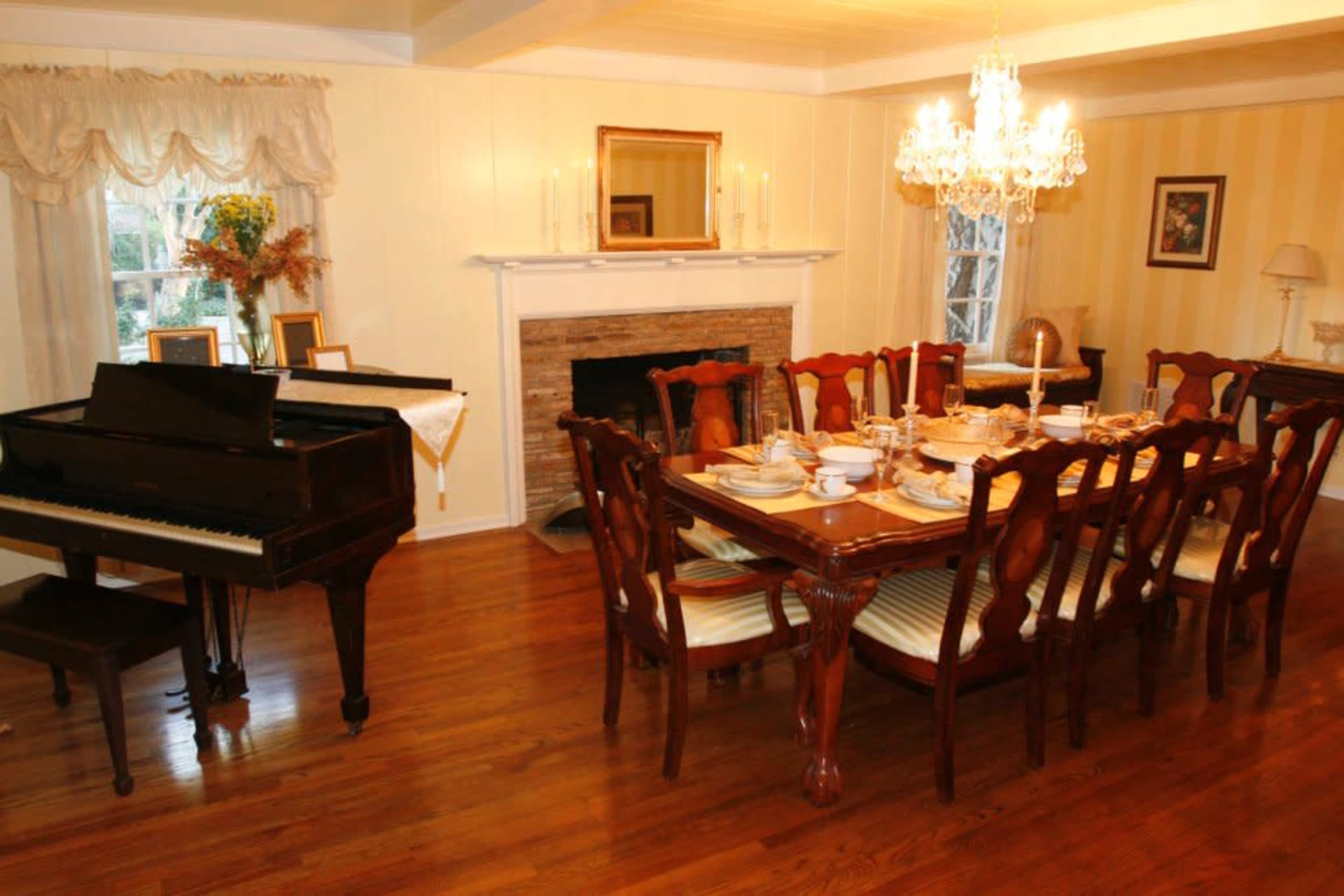 A polished wooden dining table is set for a meal in a well-lit dining room, featuring a piano and a chandelier.