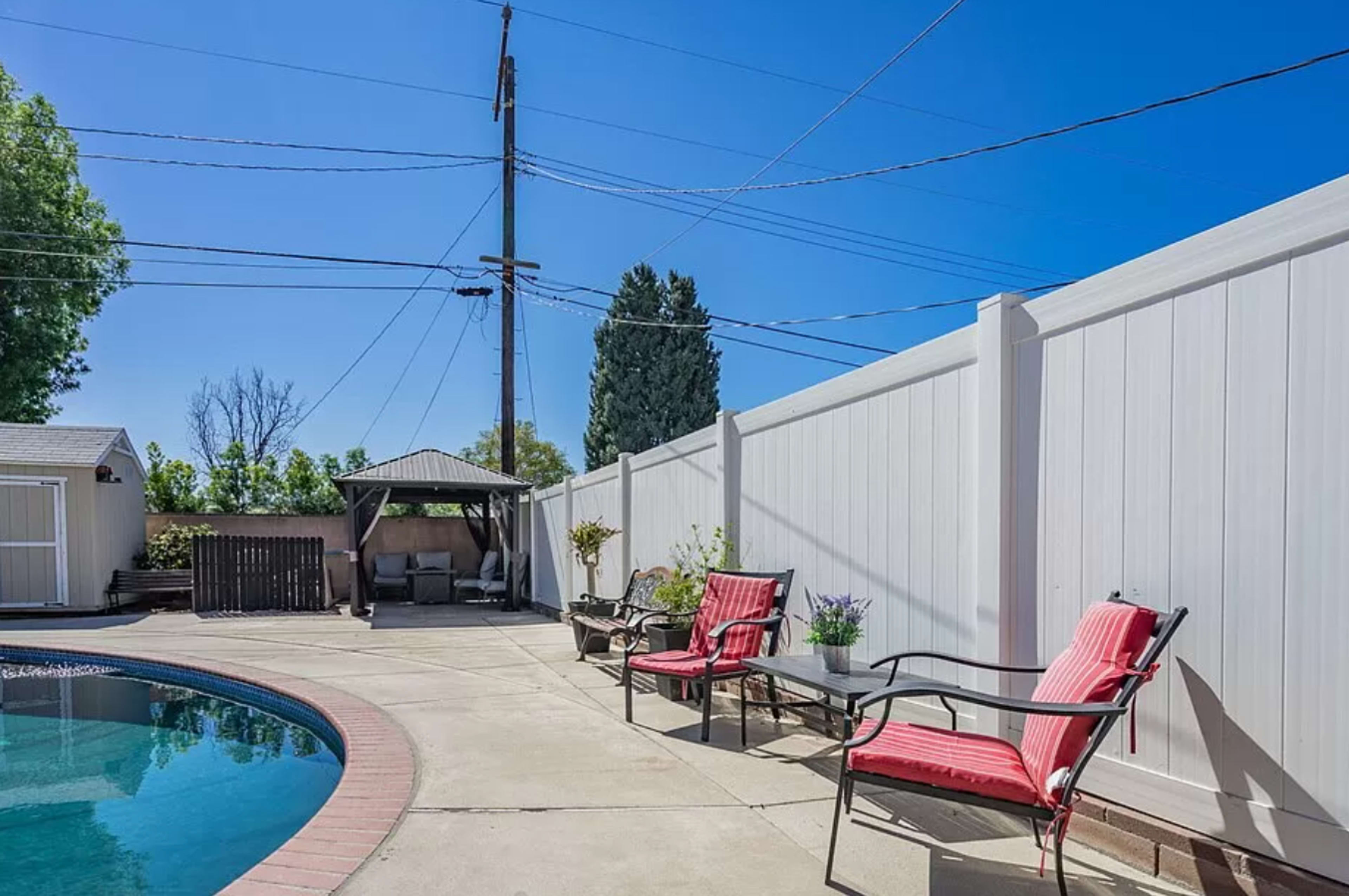 A swimming pool surrounded by a concrete patio, with two red chairs positioned nearby under clear blue skies.