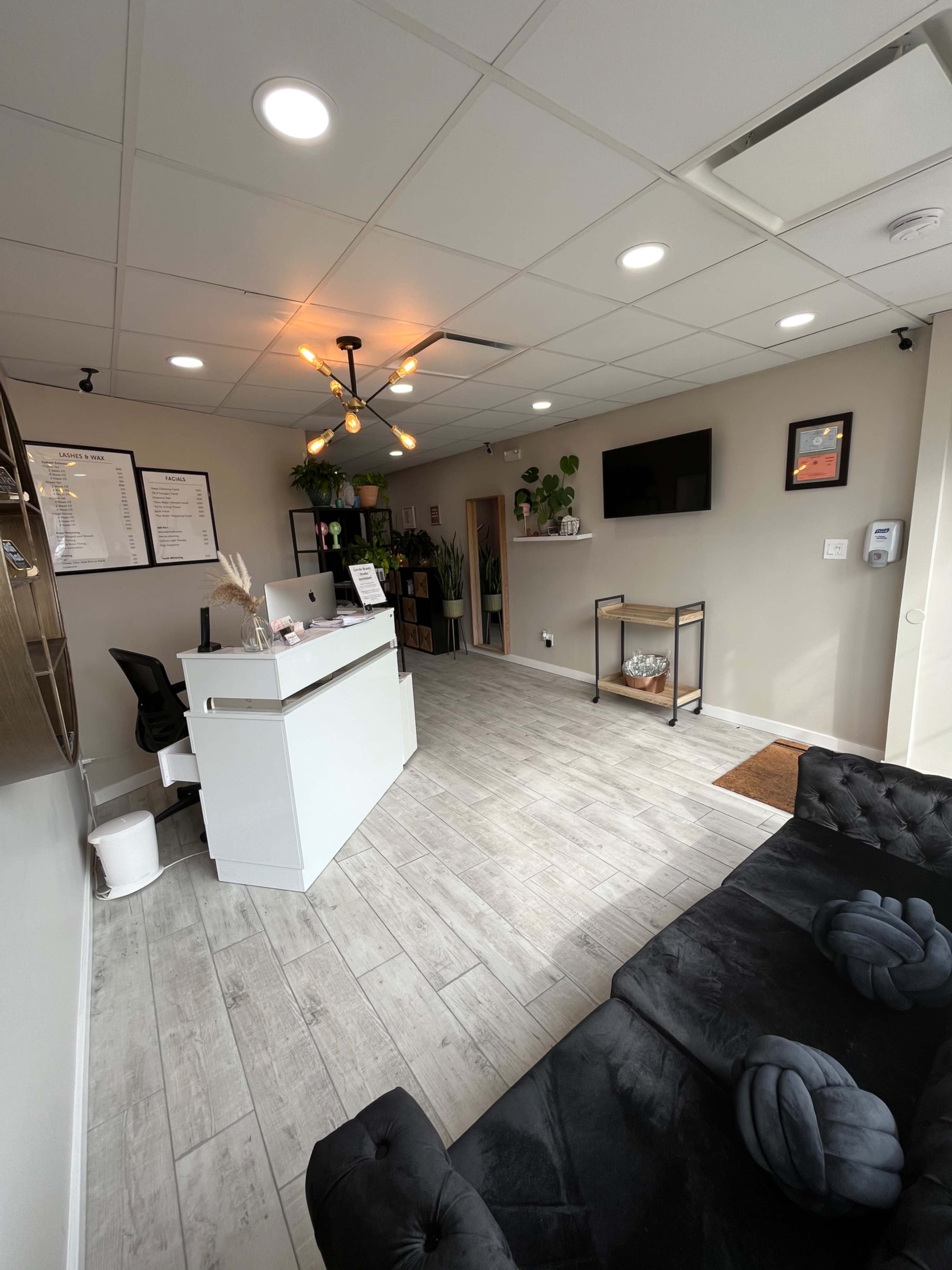 A modern reception area featuring a white front desk, a black sofa, and wall-mounted decoration in a well-lit space.