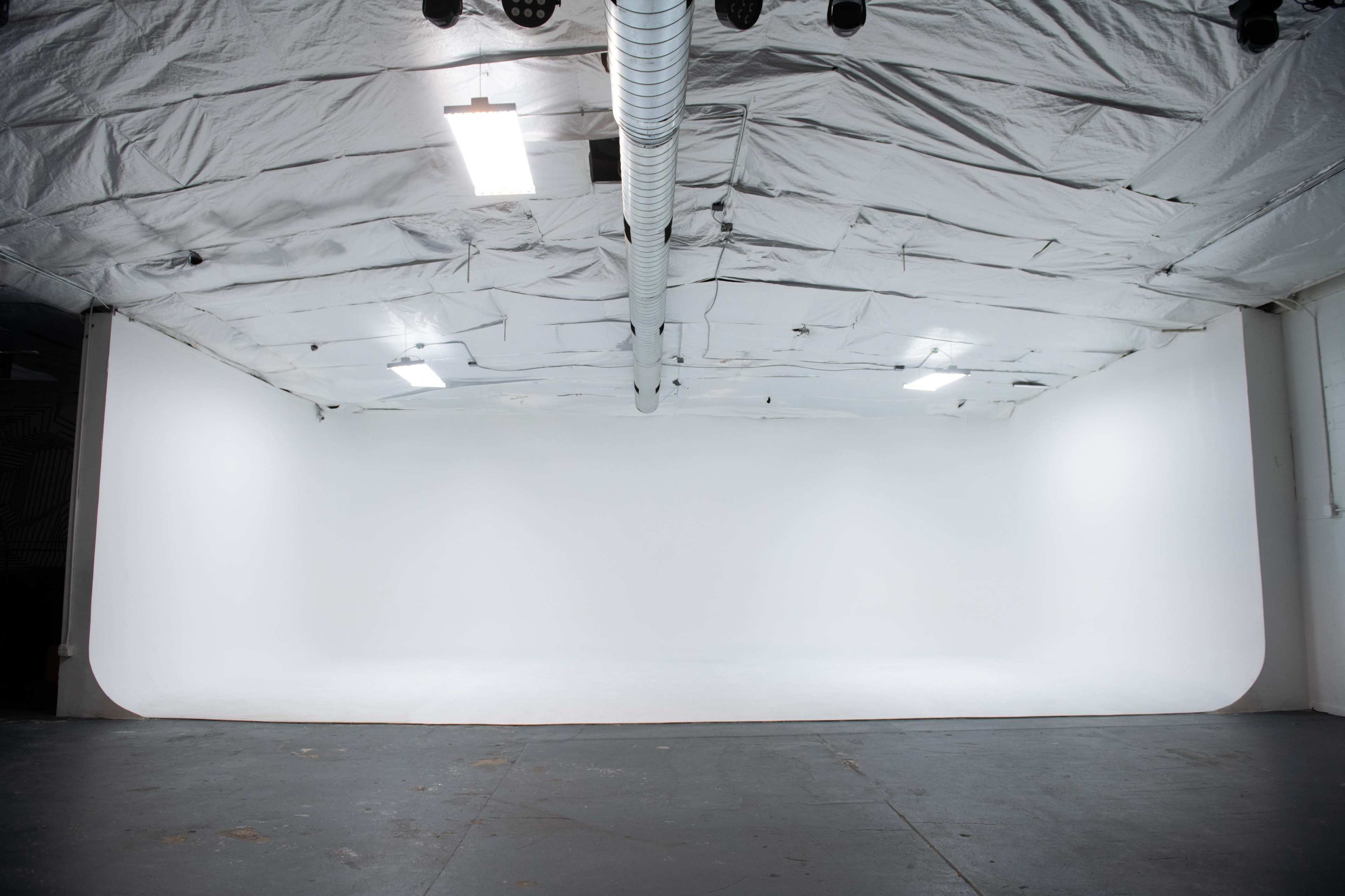 An empty studio space with a white curved backdrop, illuminated by overhead lights.