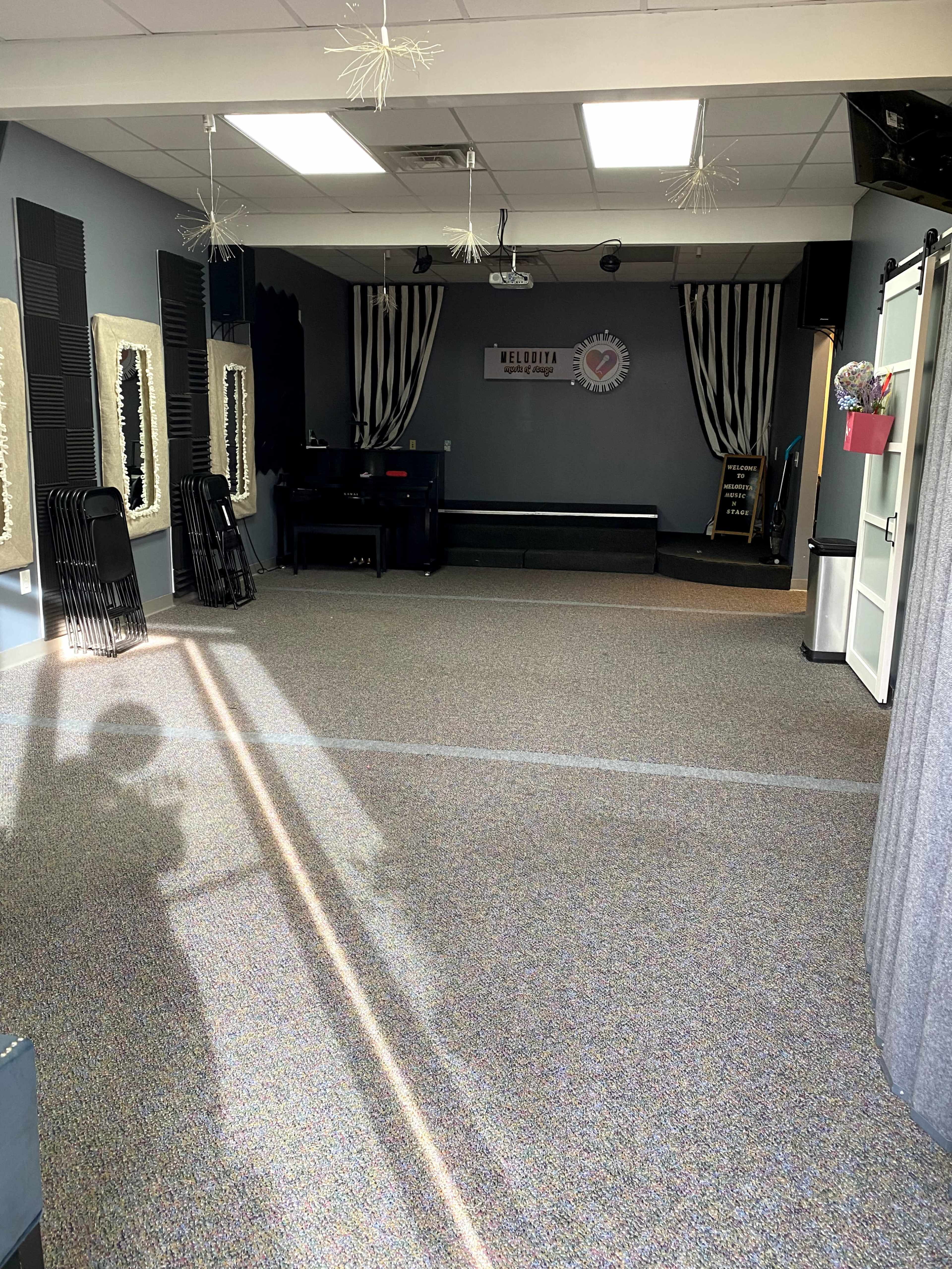 An empty interior space with gray carpeting, a stage area at the back, and decorative wall mirrors.