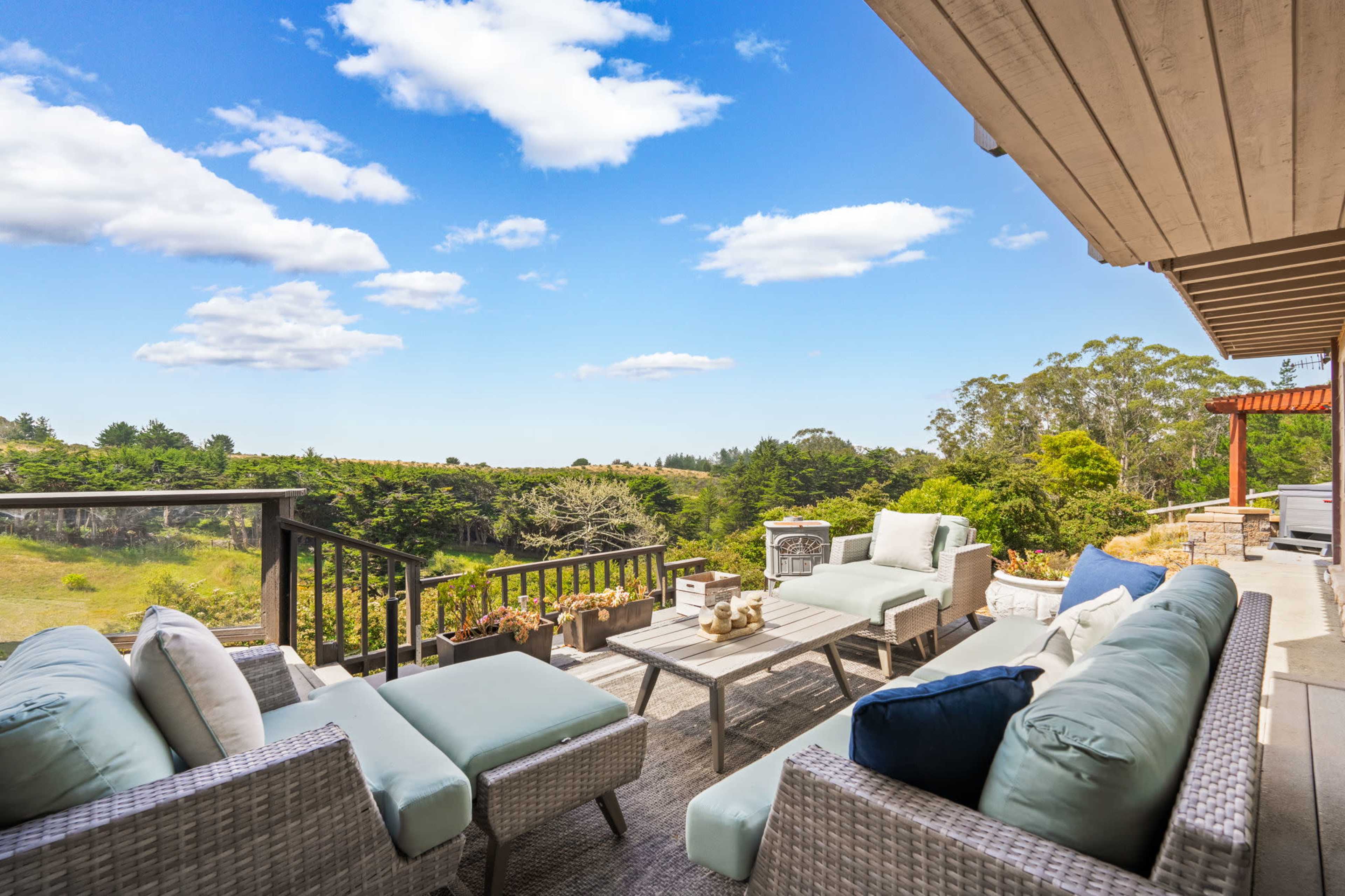 A patio with light-colored furniture overlooks a verdant landscape beneath a partly cloudy sky.
