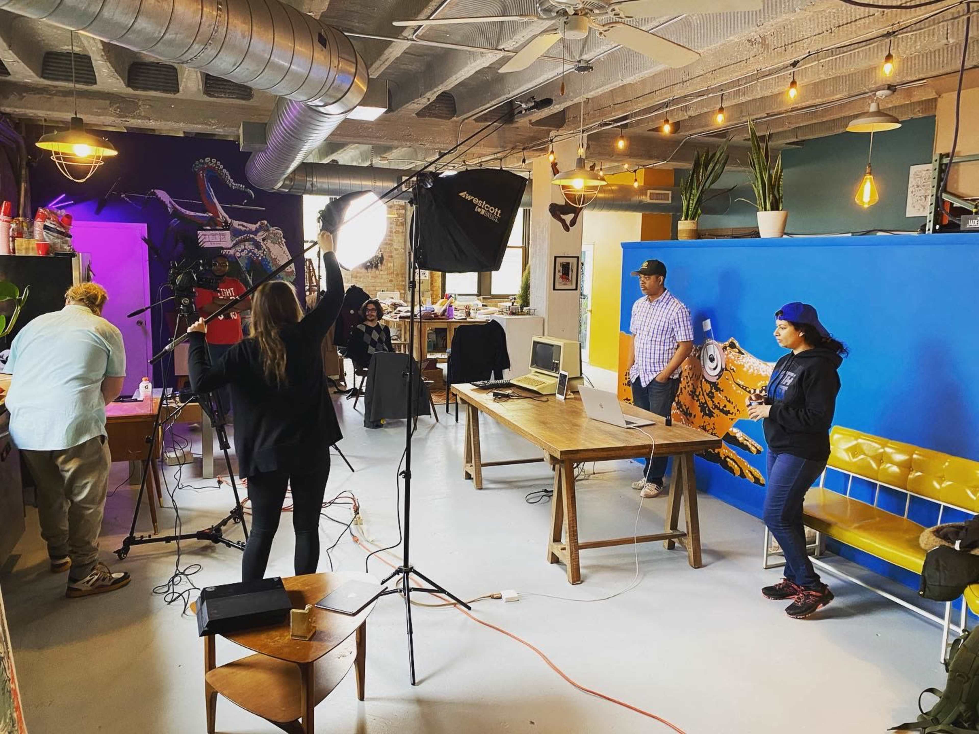 A group of people is setting up equipment for a photo or video shoot in a brightly colored creative workspace.