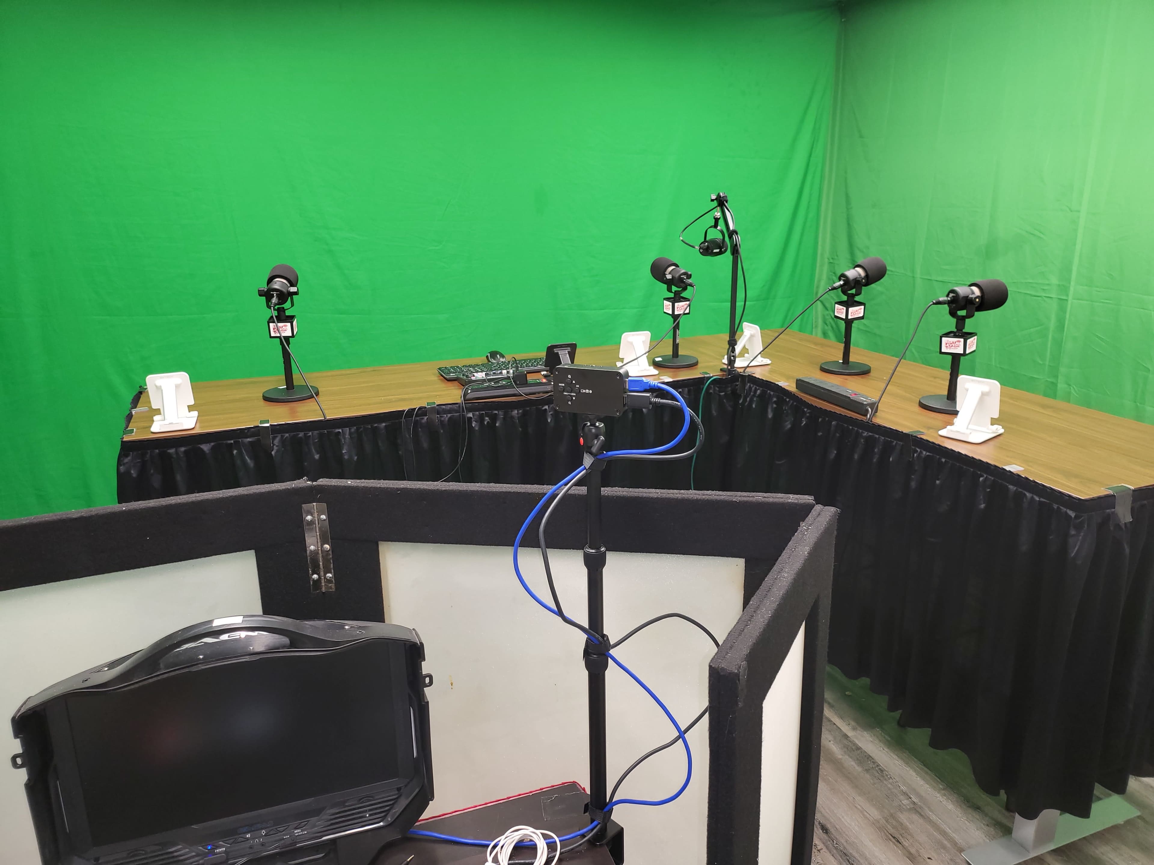 The image shows a recording studio with multiple microphones on stands, a table, and green screen backdrop.