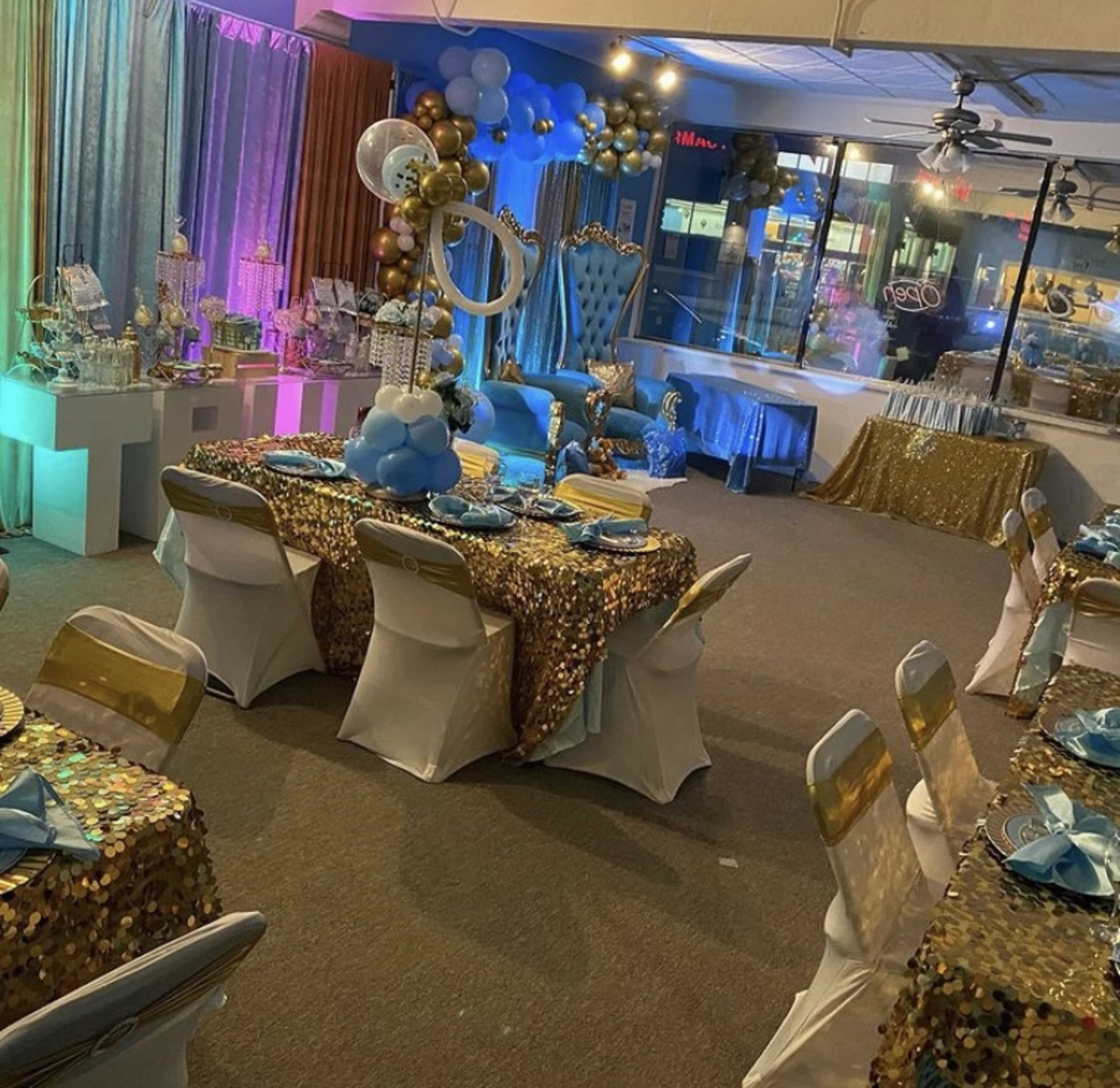 A banquet hall decorated for an event, featuring tables with sequined tablecloths, balloons, and various decorative arrangements.