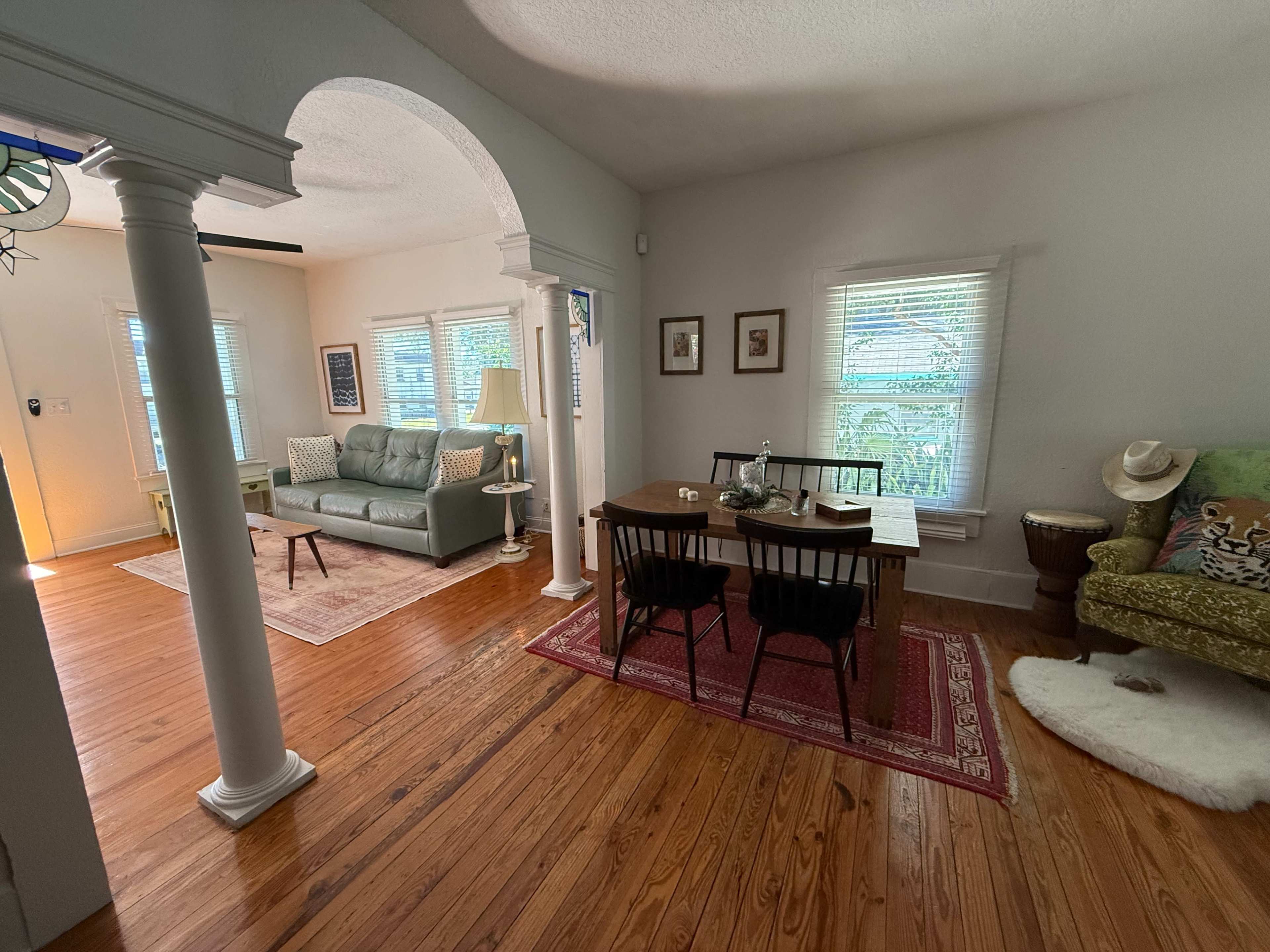 The image shows a cozy living space featuring a seating area with a green couch, a wooden dining table, and various decorative items on a hardwood floor.