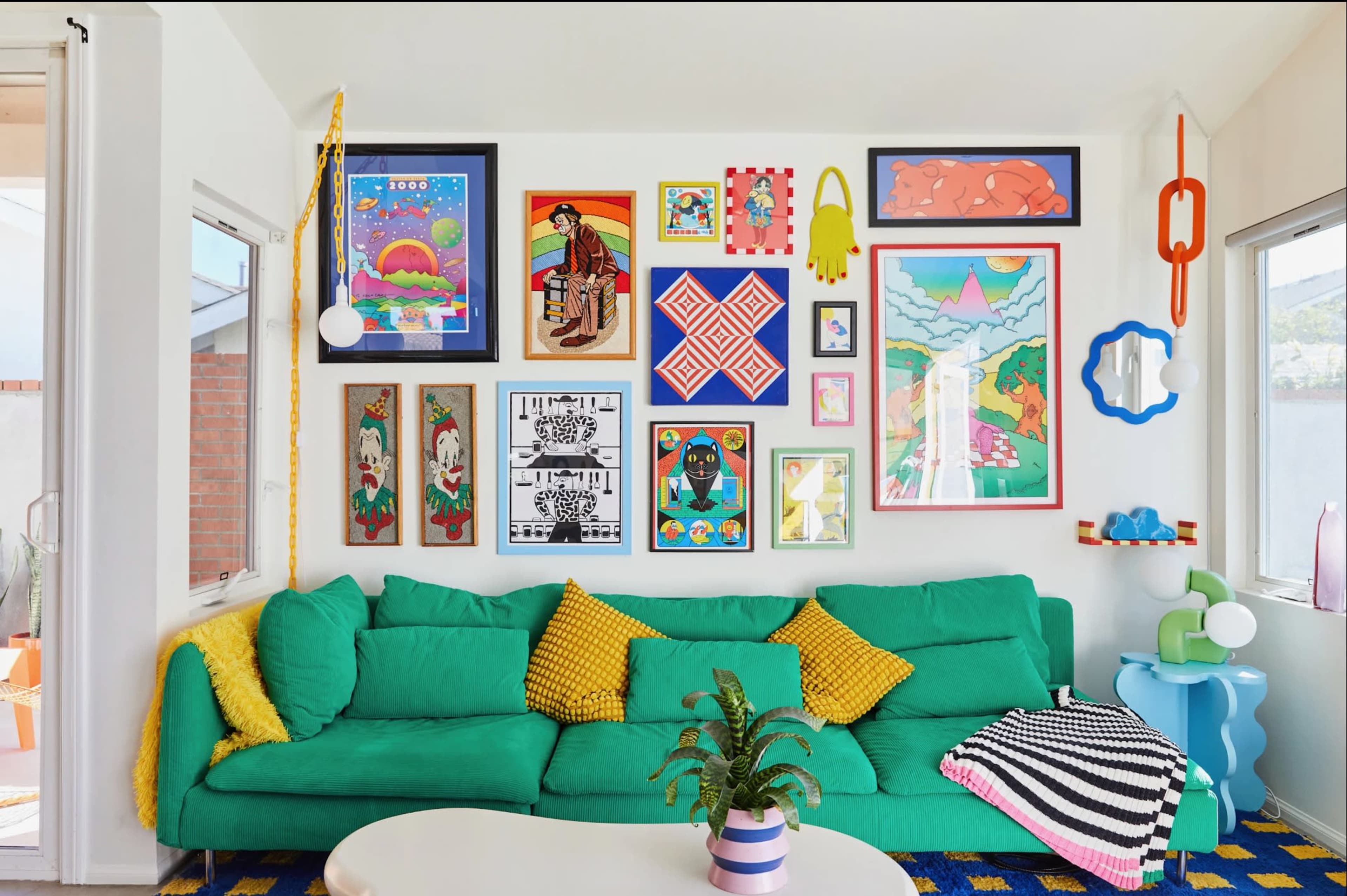 The image shows a vibrant living room with a green sofa adorned with yellow decorative pillows, a round coffee table, and a wall filled with various colorful framed artworks.