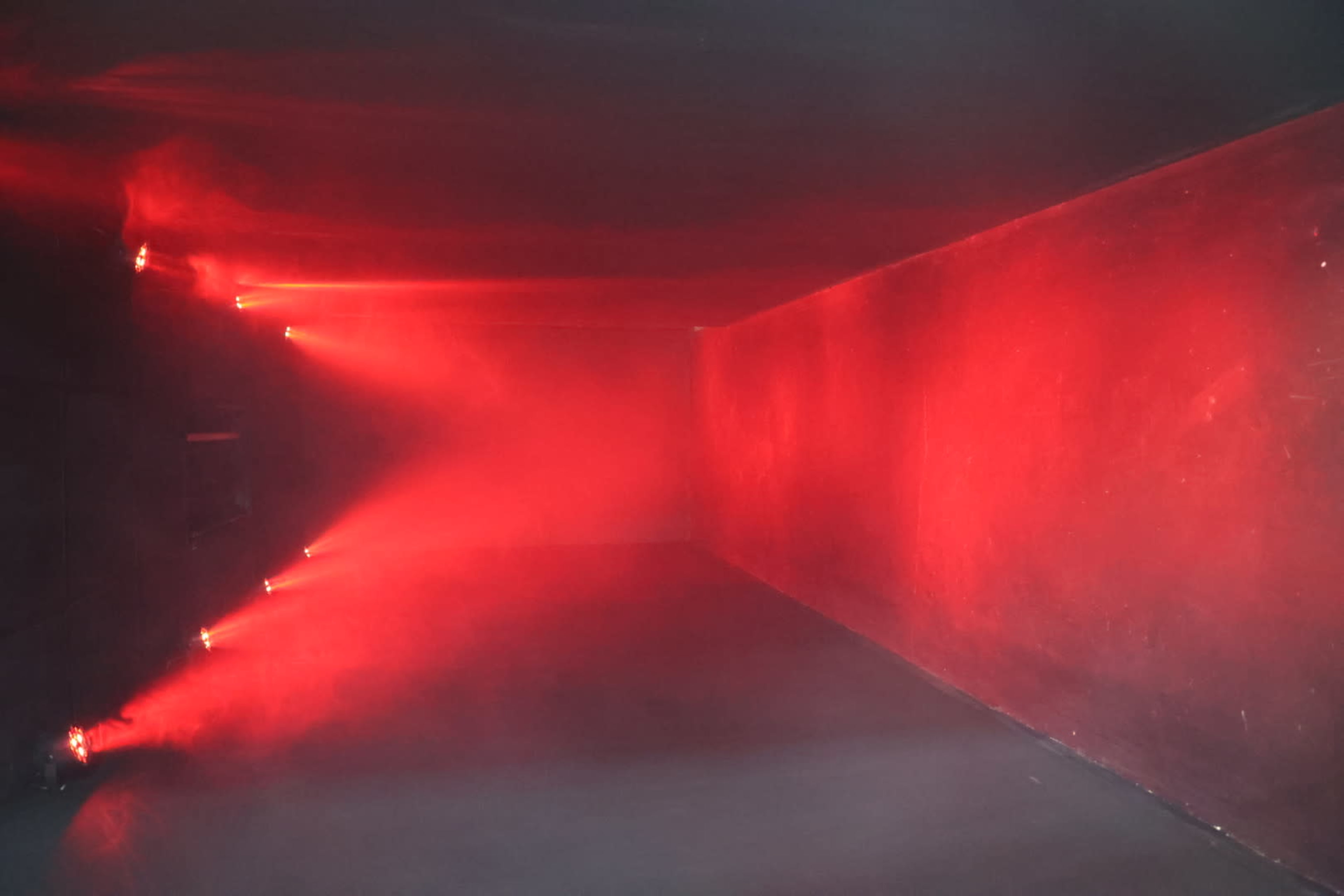 A dimly lit room with red beams of light illuminating the corners and walls, creating a hazy atmosphere.