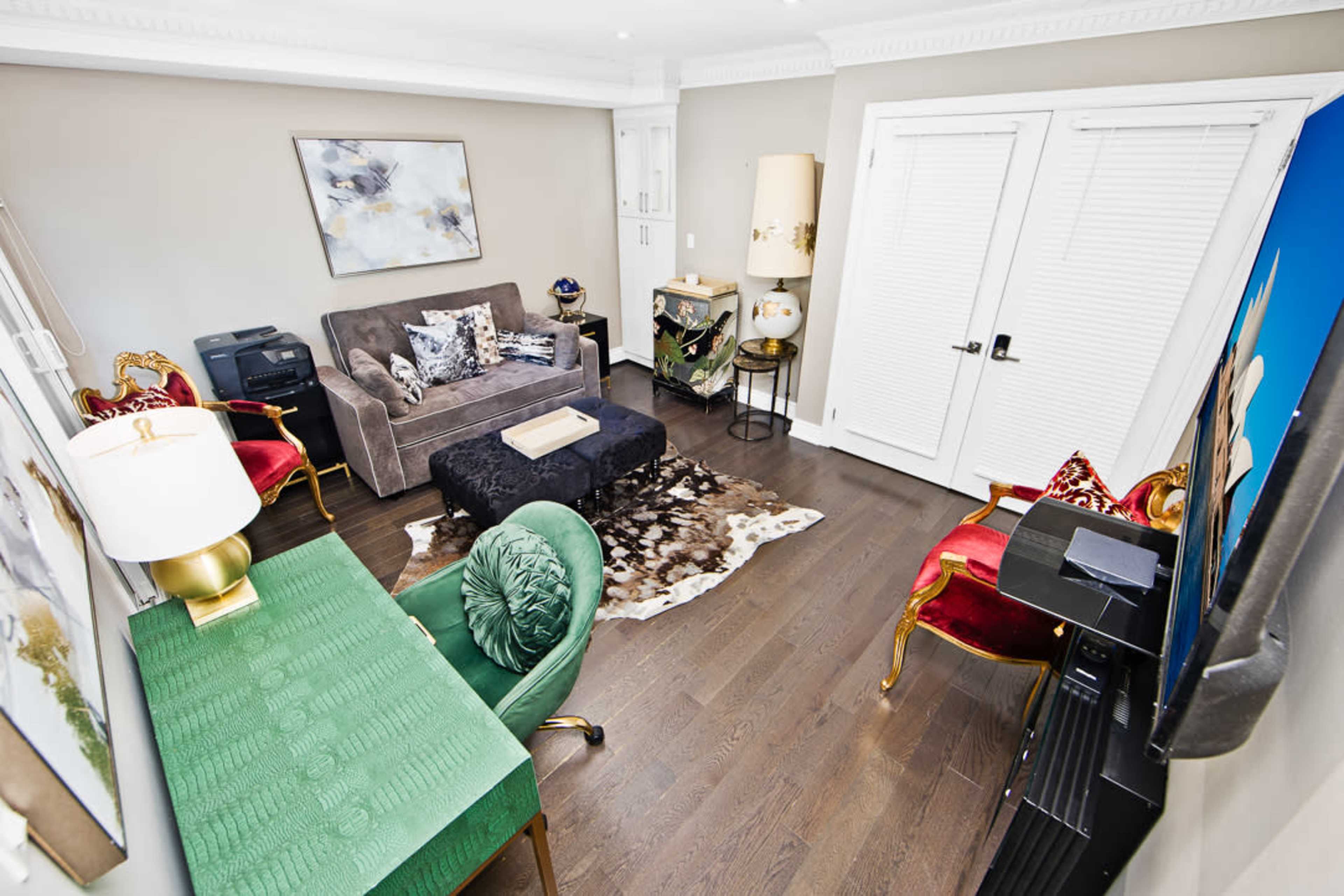The image shows a small living room featuring a sofa, two armchairs, a coffee table, and a desk, all arranged around a decorative rug.