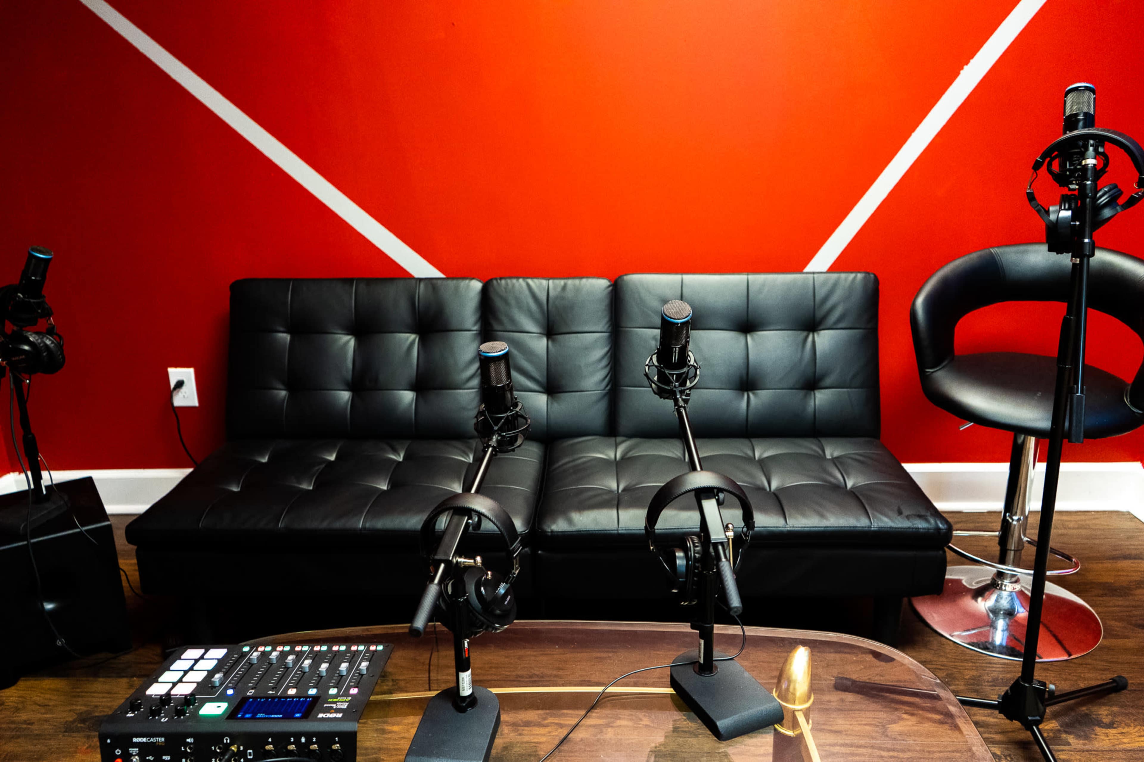 The image shows a black couch with two microphones mounted on stands in front of it, set against a red wall with white diagonal lines.