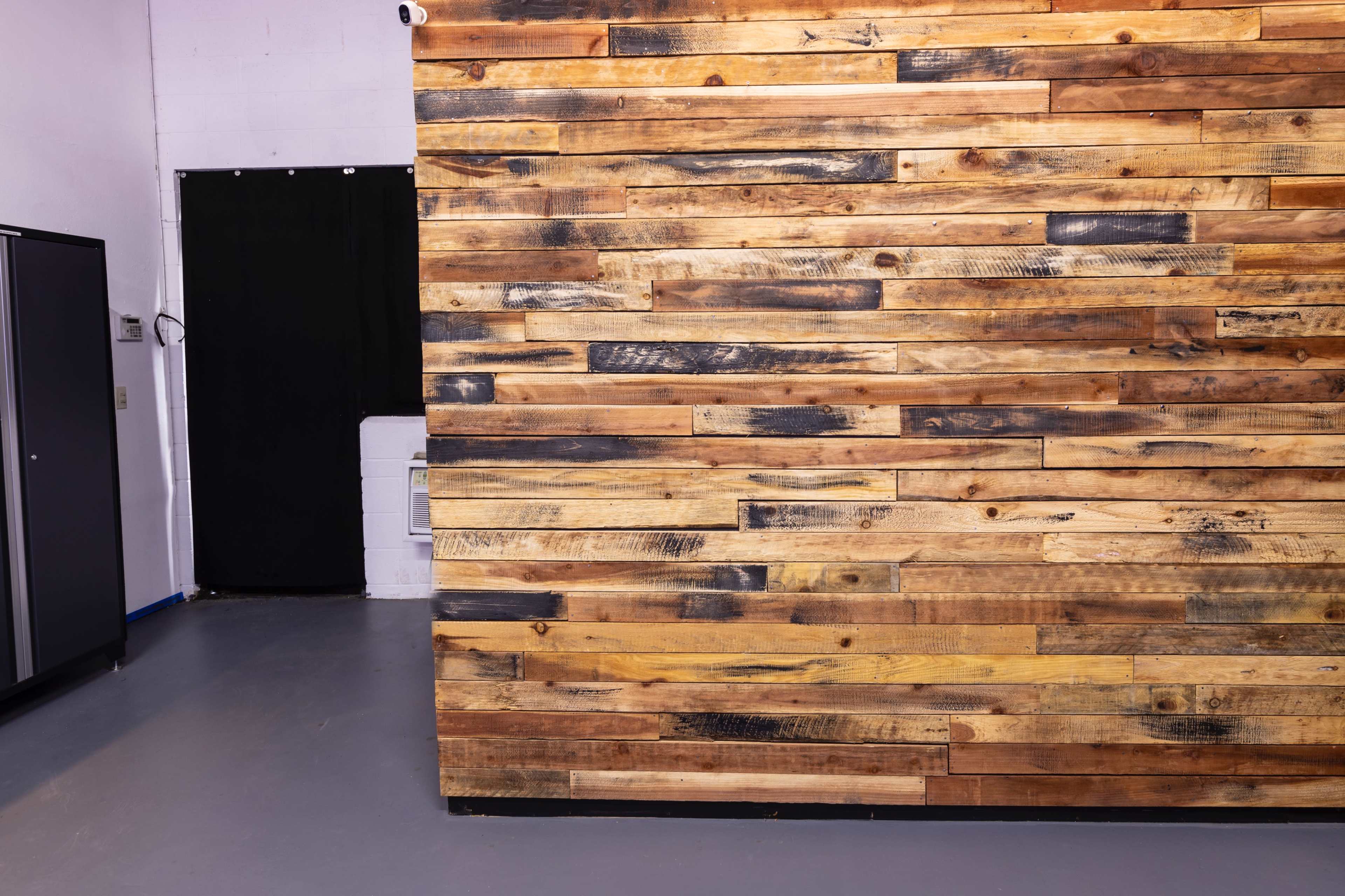 A wooden wall made of variously colored planks with a dark curtain and a metal cabinet visible in the background.