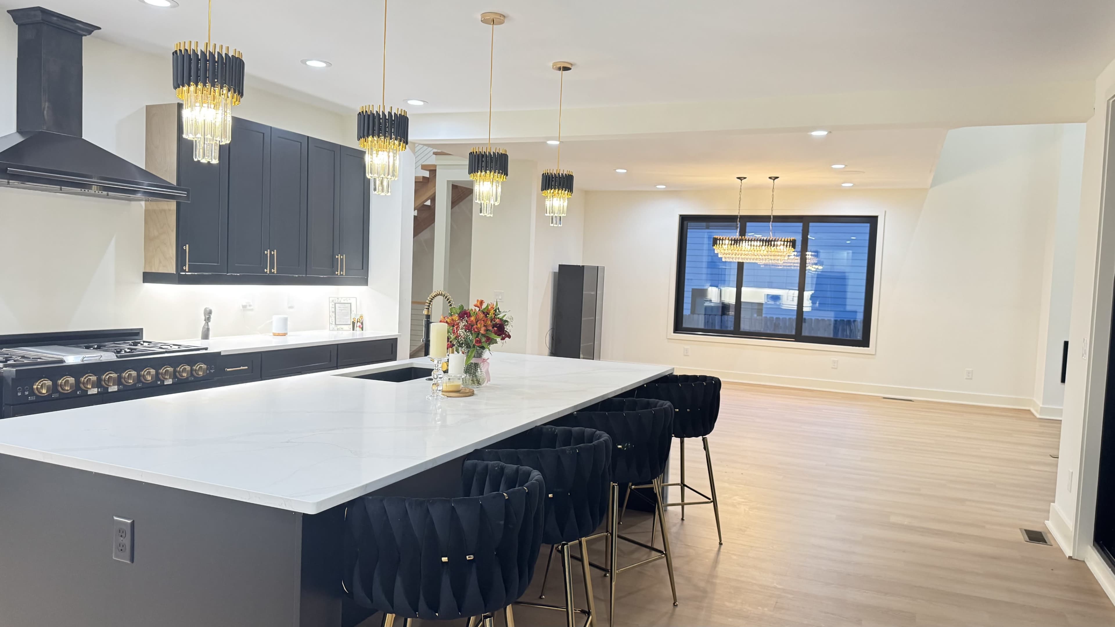 The image shows a modern kitchen featuring a large island with bar seating, sleek black cabinetry, and pendant lighting.
