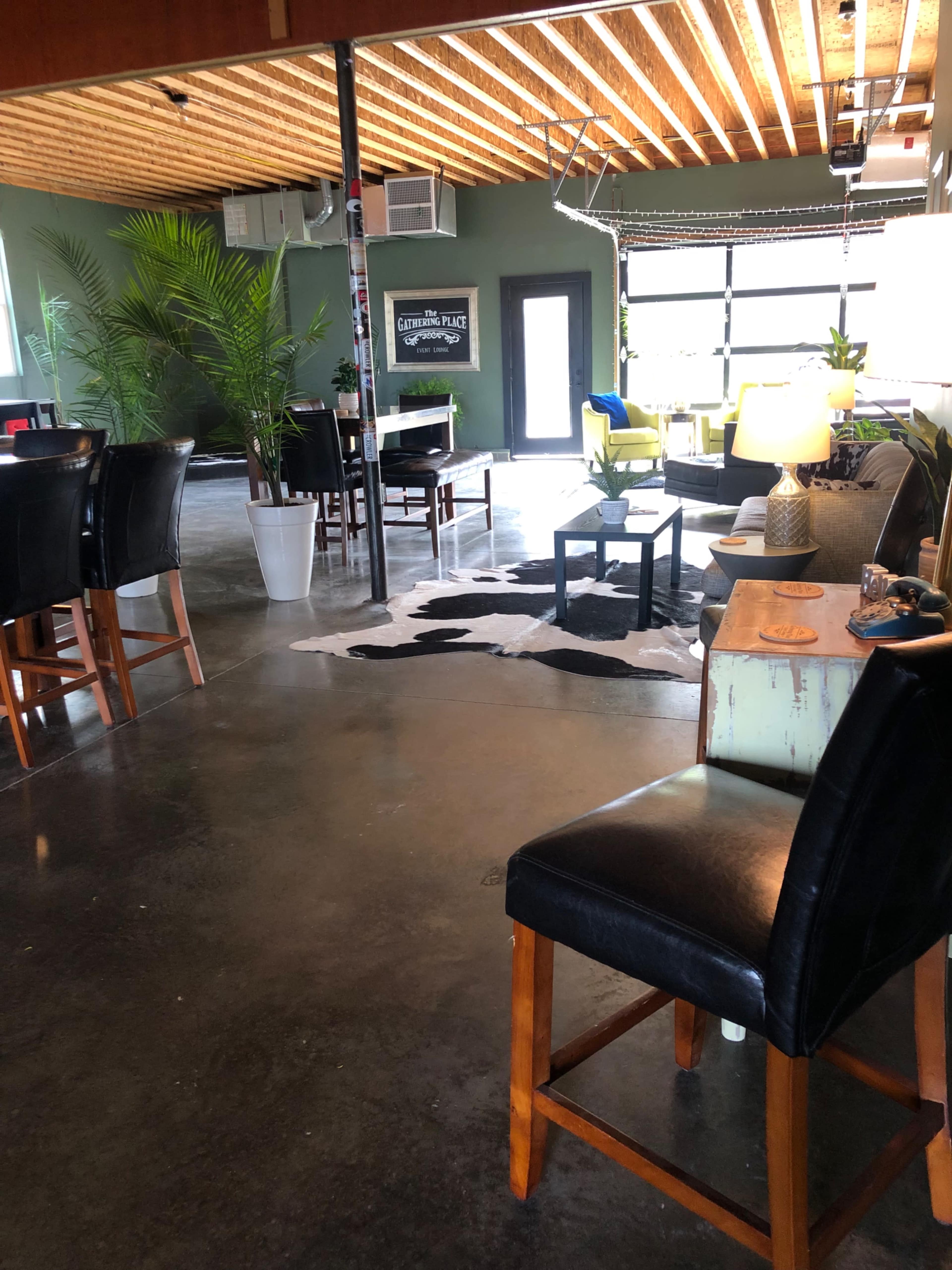 The image shows a modern interior space with a polished concrete floor, wooden beams, and various seating arrangements, including high chairs and a sofa.