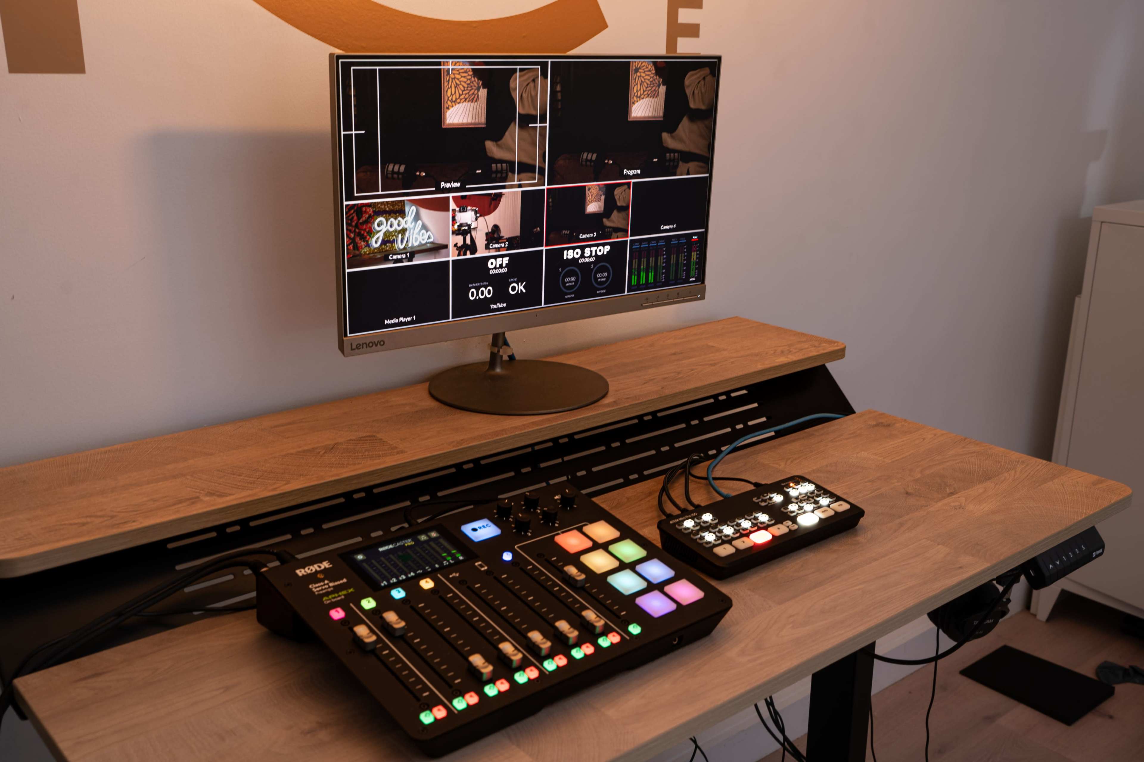 A monitor displays multiple camera feeds while a control interface with buttons and sliders sits on a wooden desk.