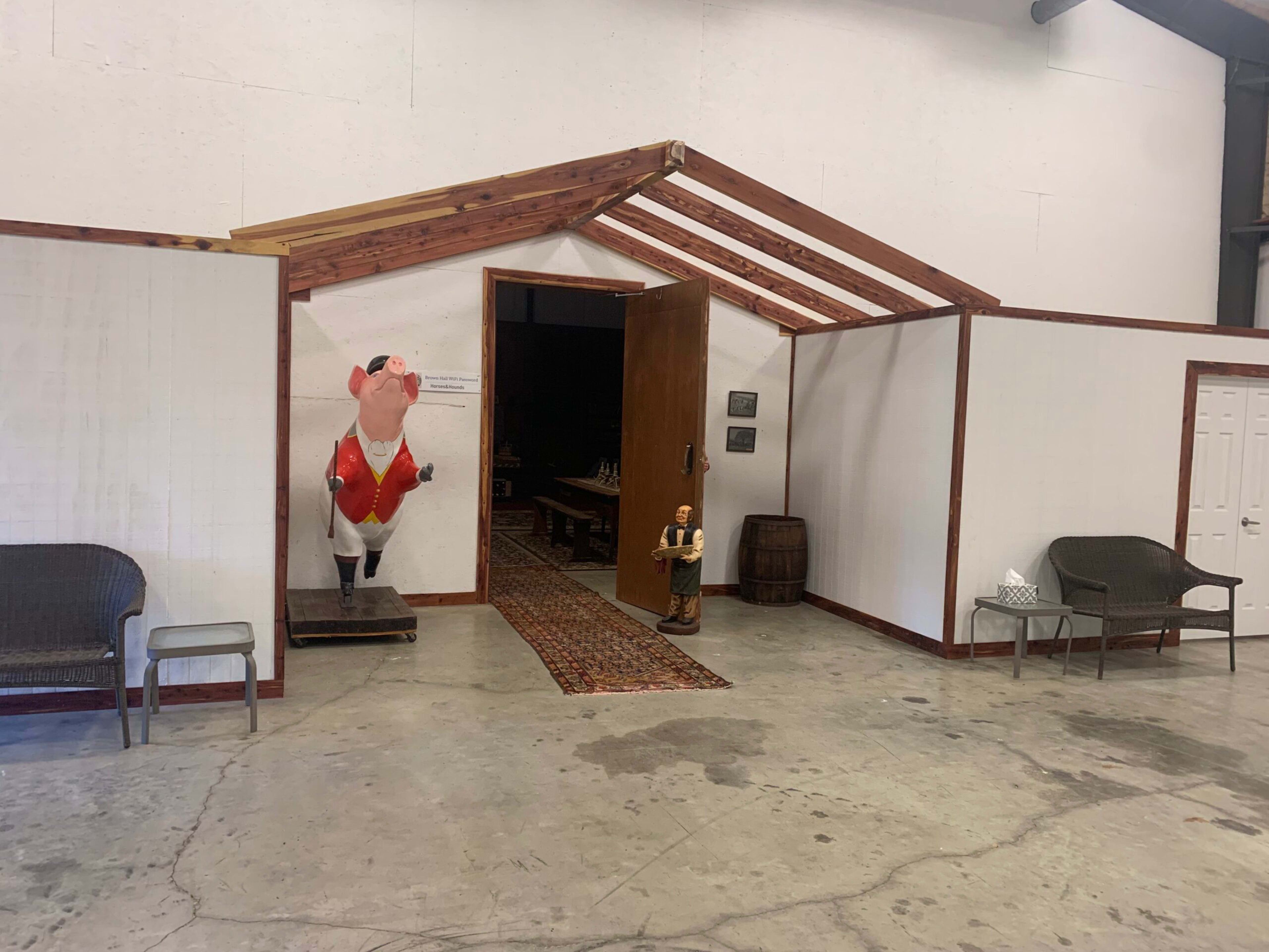 The image shows an interior space with a partially constructed wooden structure featuring a door leading to another area, flanked by a decorative pig statue and two chairs on either side.