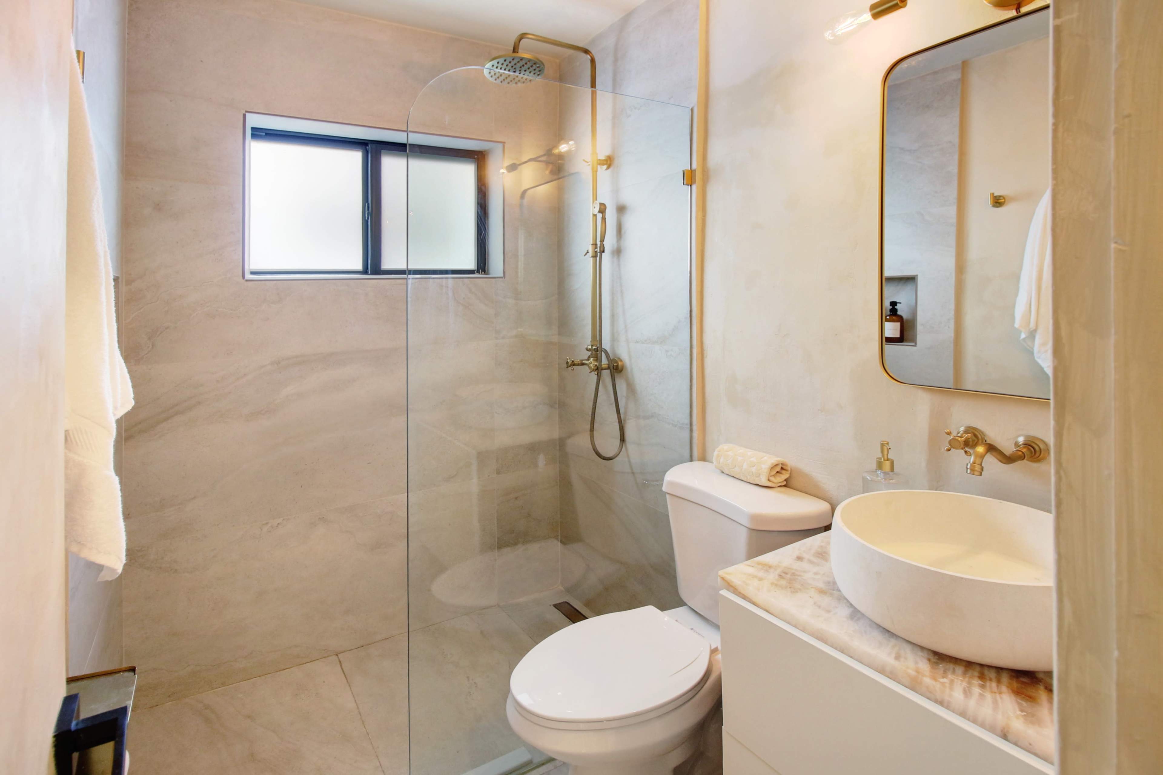 A modern bathroom with a glass shower enclosure, a toilet, a round sink on a marble countertop, and a large mirror.