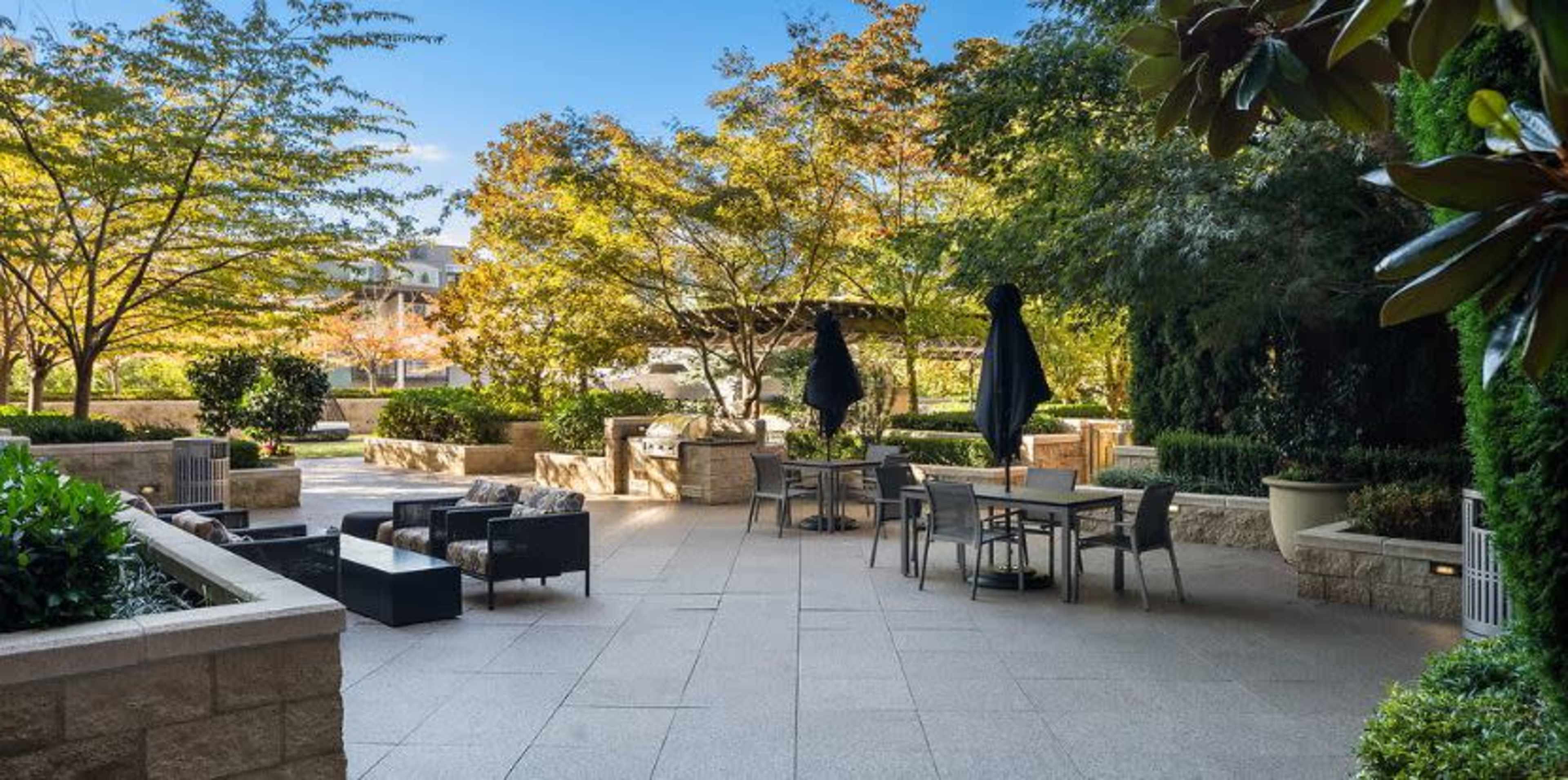 A landscaped outdoor patio area featuring seating, tables, and lush greenery.