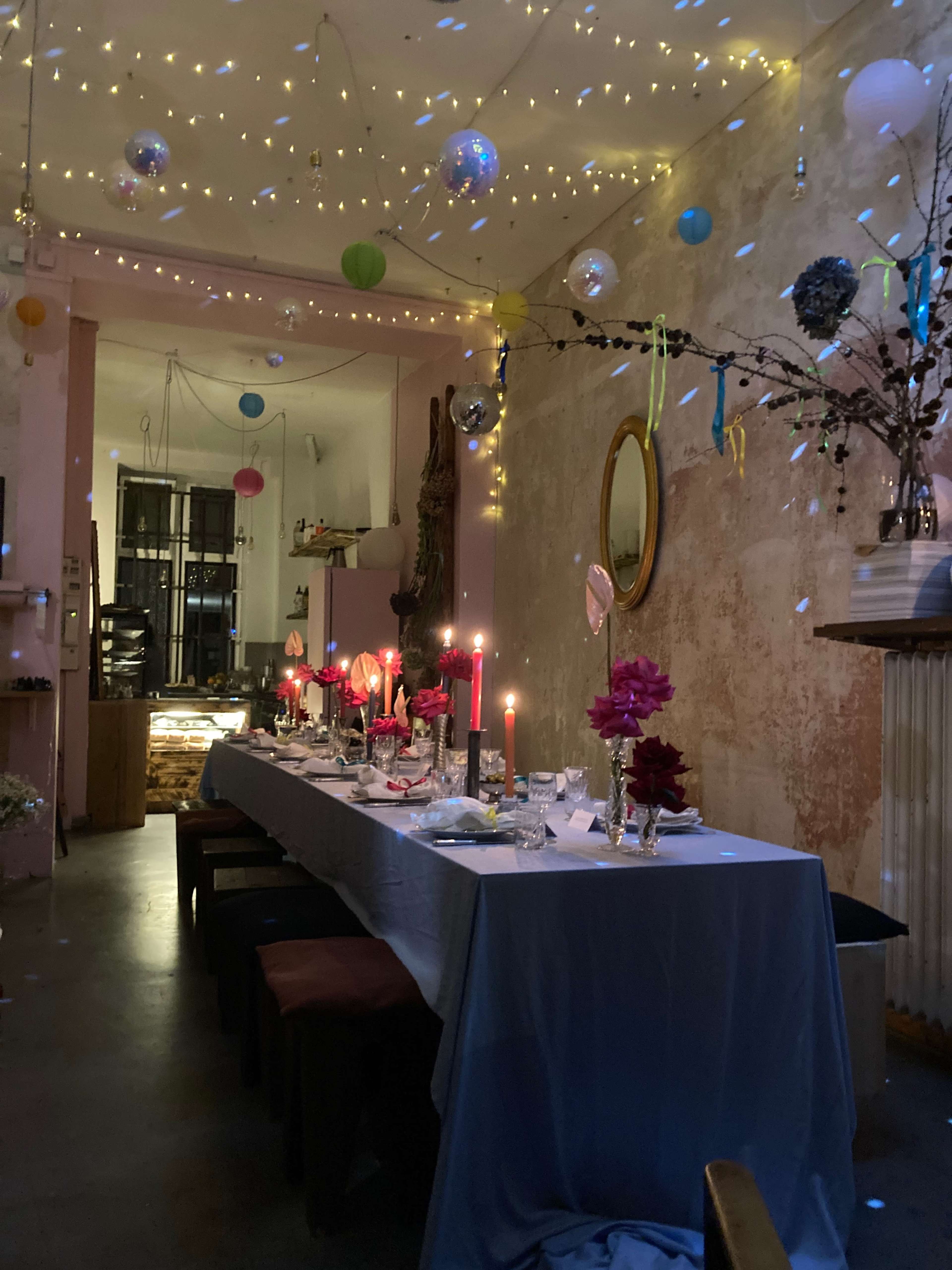A long table is set with candles and decorations in a dimly lit room adorned with hanging decorations and soft lighting.