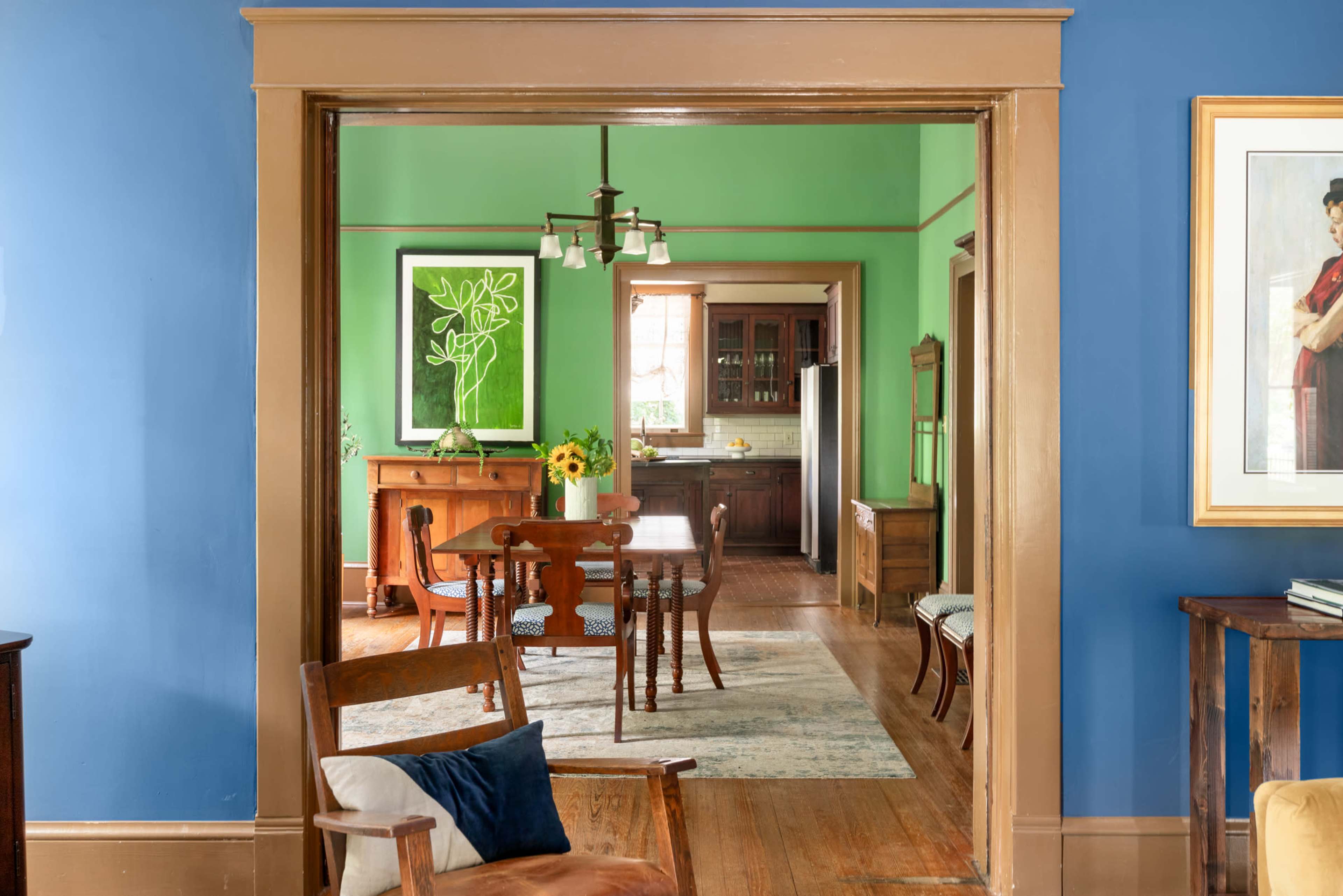 The image shows a brightly colored room with blue walls and a green room visible through an open doorway, featuring wooden furniture and a dining area.