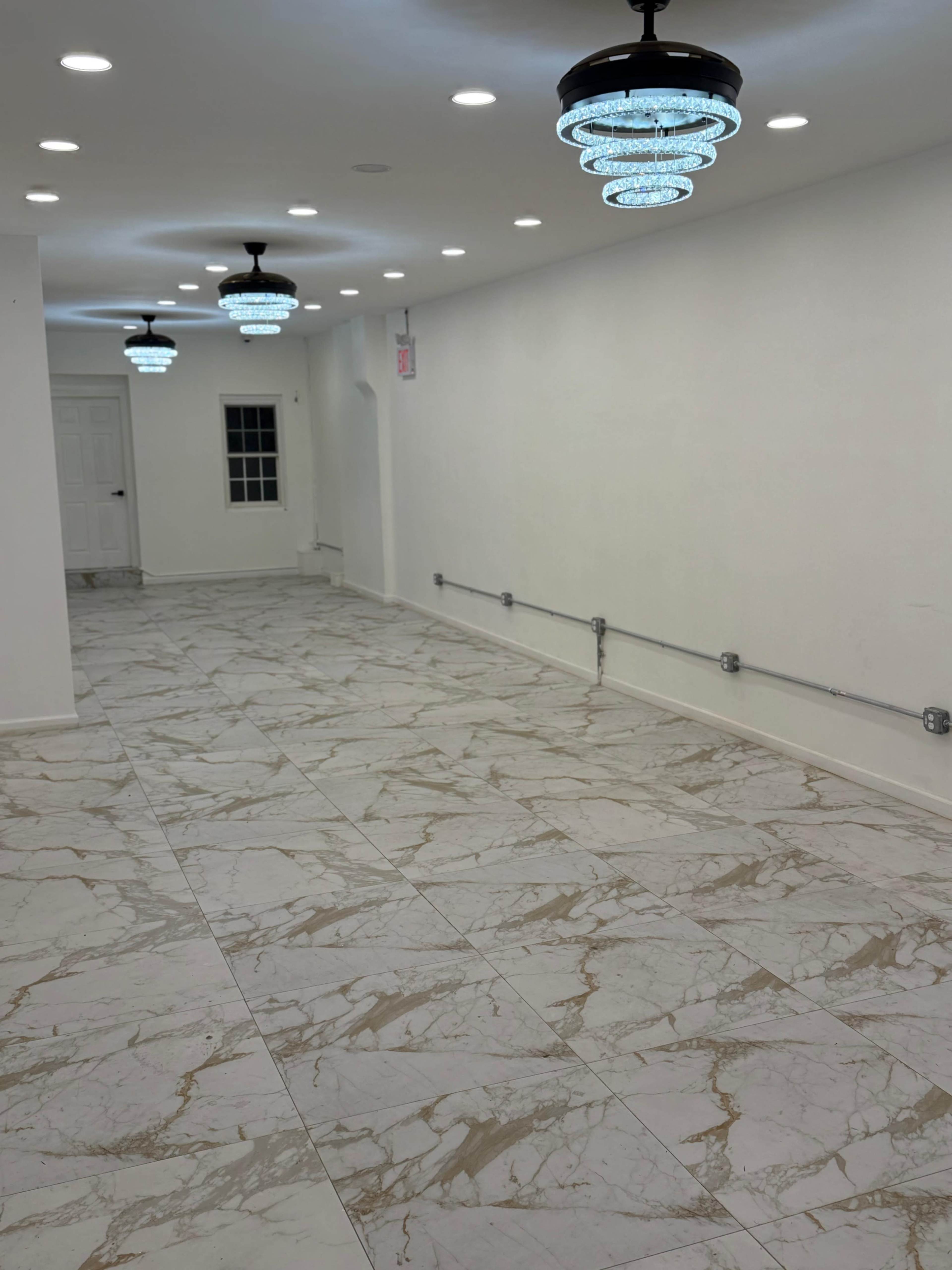 The image shows a spacious, empty hallway with white walls and marble-patterned flooring, illuminated by hanging light fixtures.