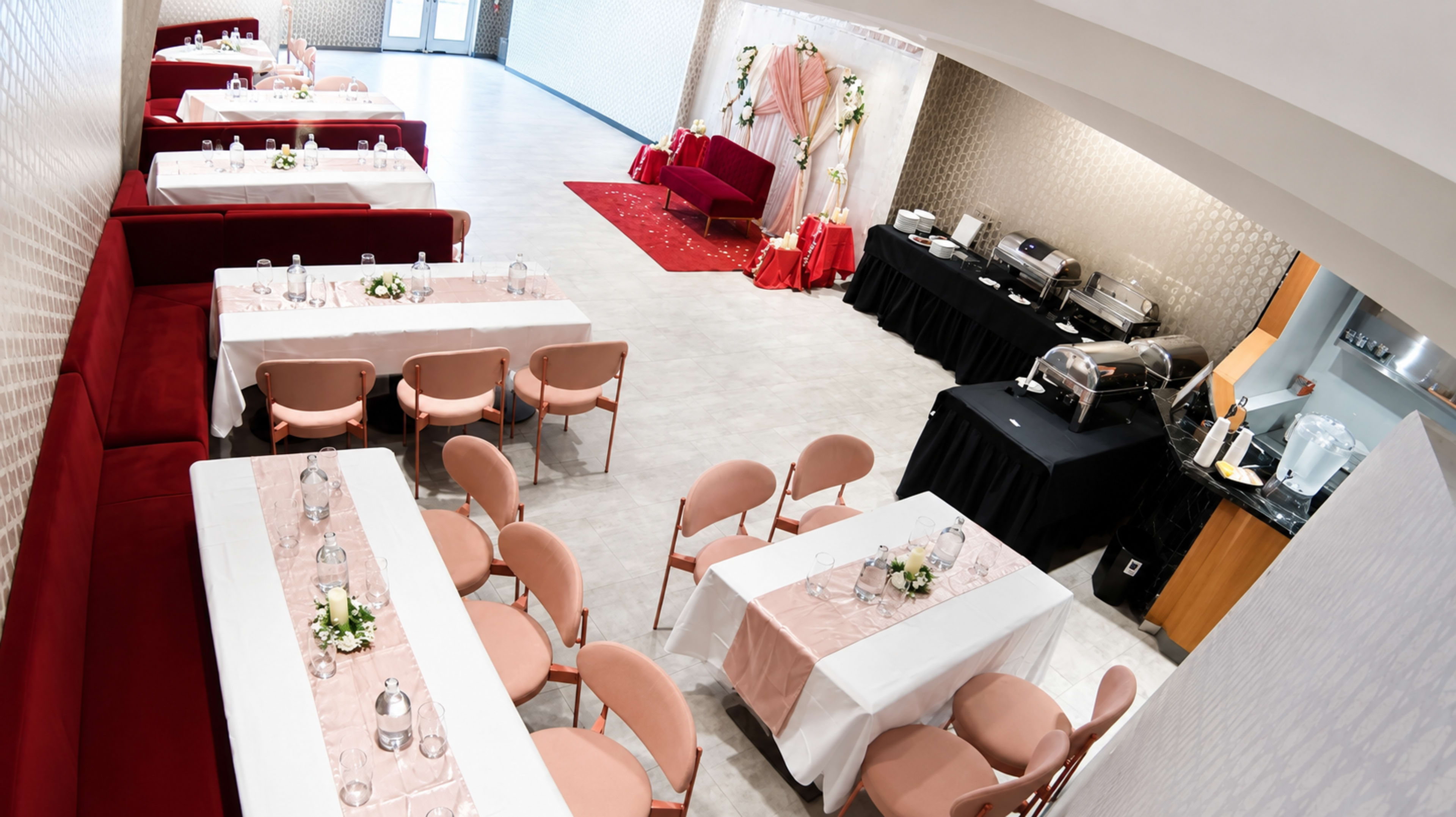 The image shows a spacious dining area set with tables and chairs, featuring decorations for an event, including a red sofa and a buffet setup.