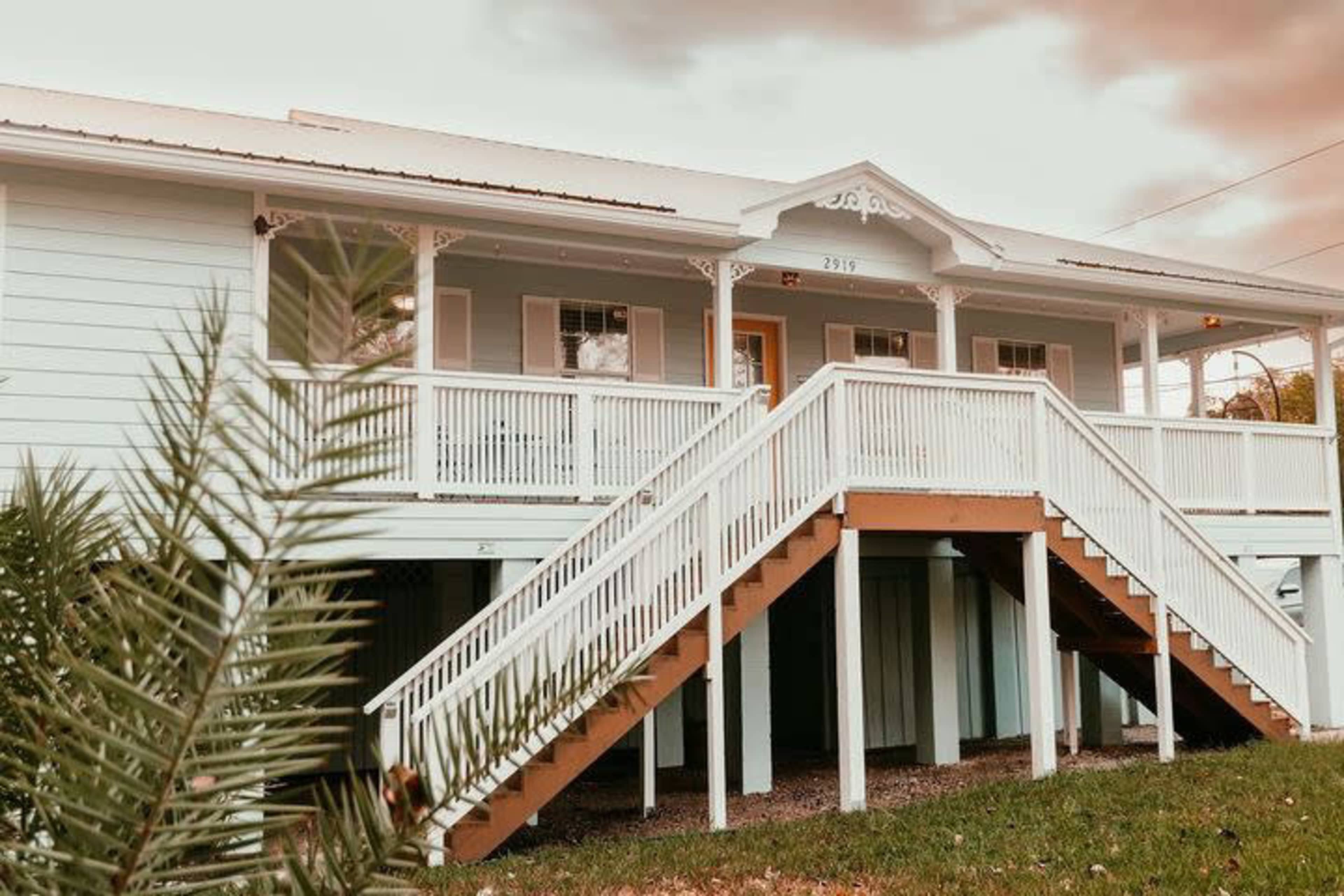 A two-story house with a light blue exterior and a white wooden staircase leading to the entrance.