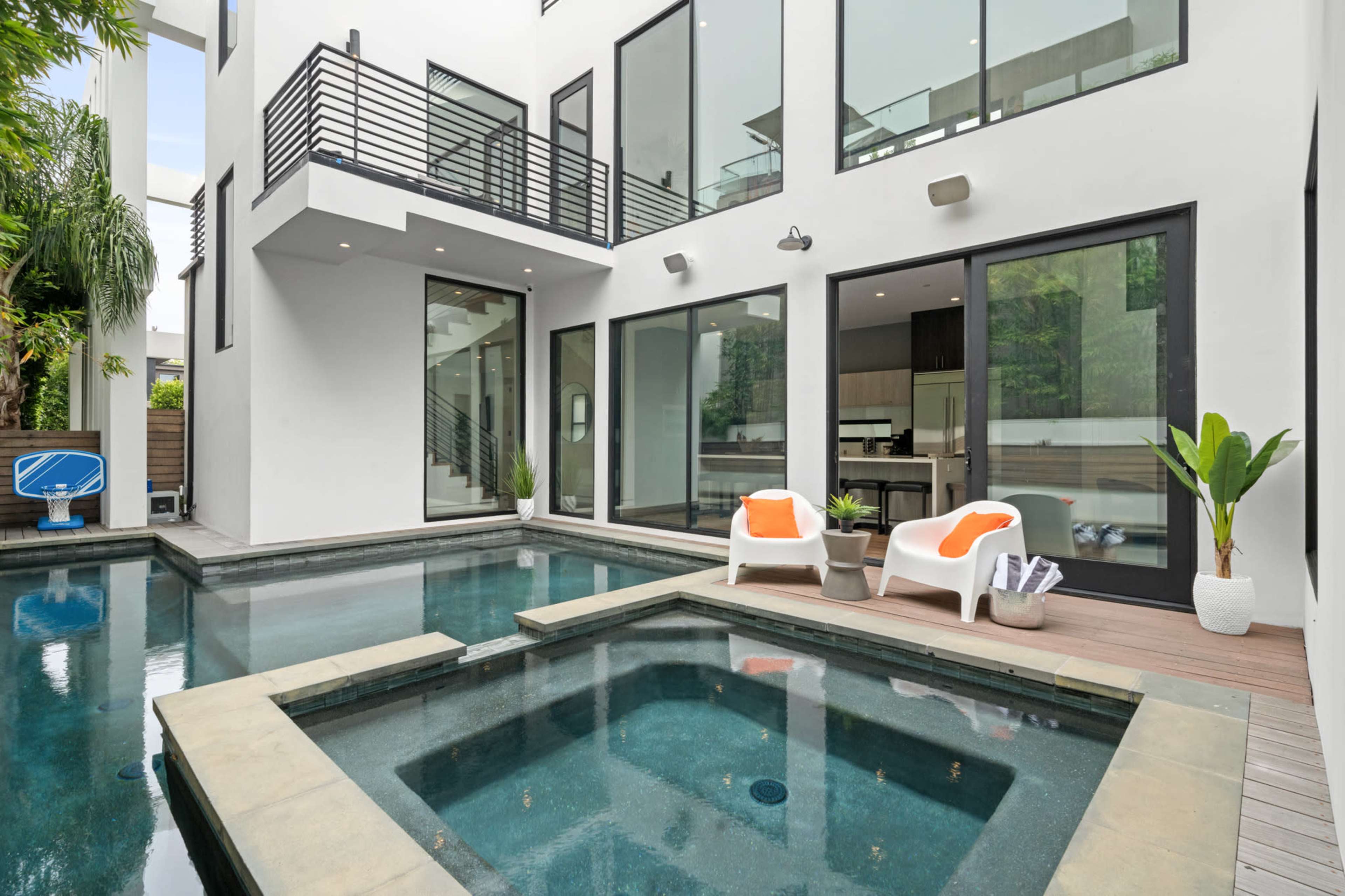A modern home with large glass windows surrounding a pool area, featuring a hot tub and outdoor seating.
