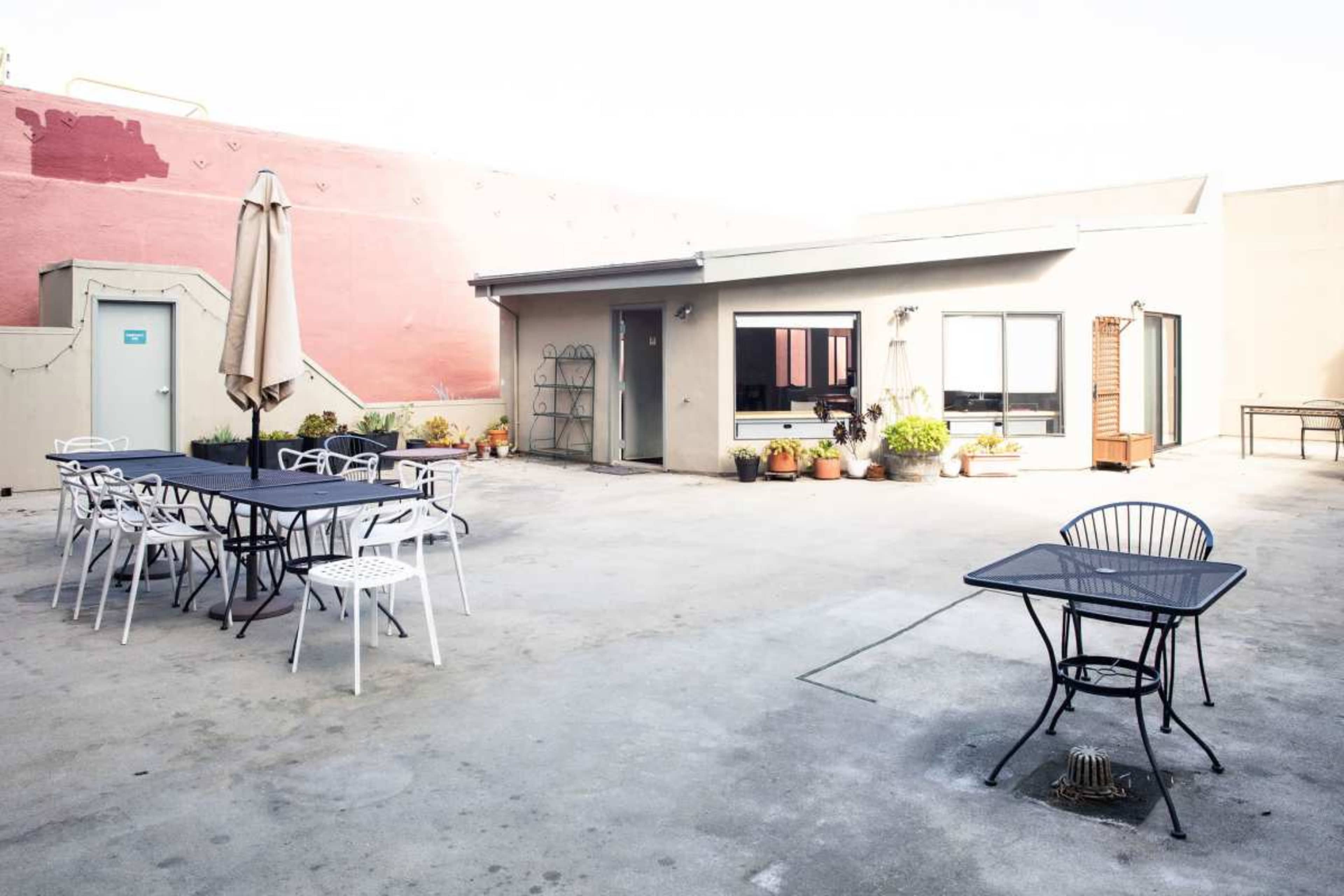 The image shows a rooftop patio with several tables and chairs arranged around a small building, surrounded by potted plants.