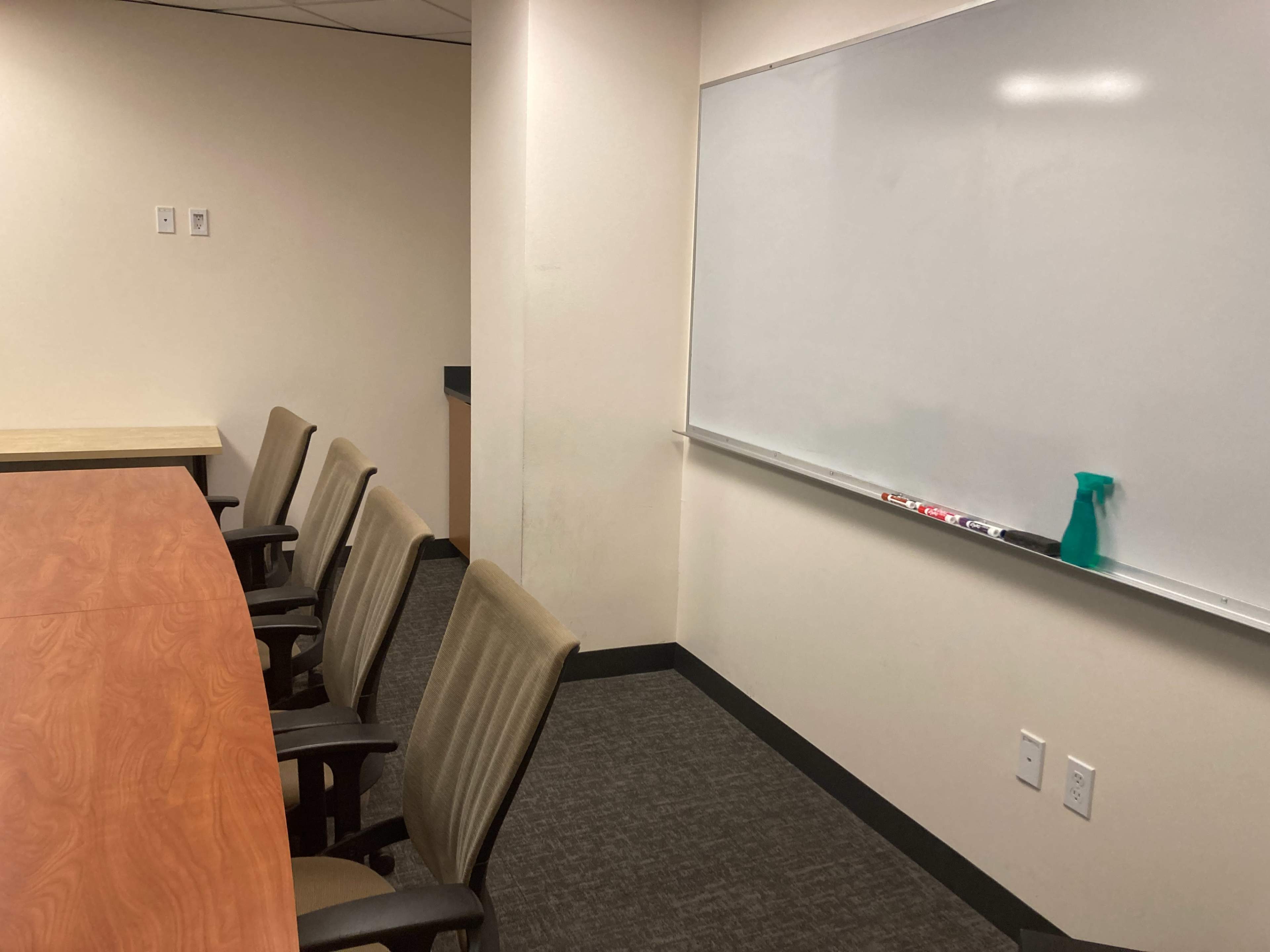 A conference room with a long table and several chairs on one side, adjacent to a whiteboard mounted on the wall.