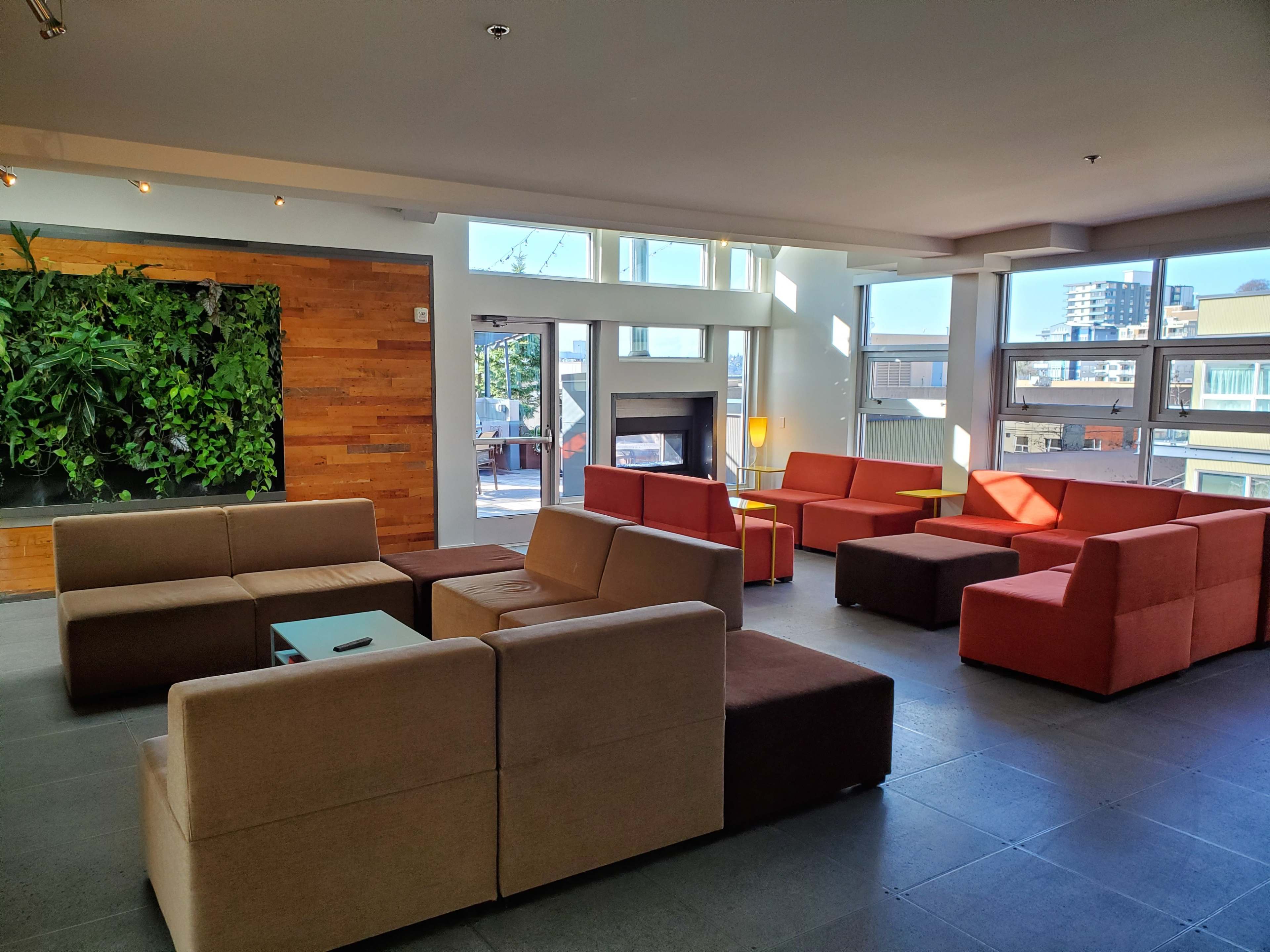 A modern lounge area featuring several sofa arrangements in neutral and warm colors, illuminated by natural light from large windows.