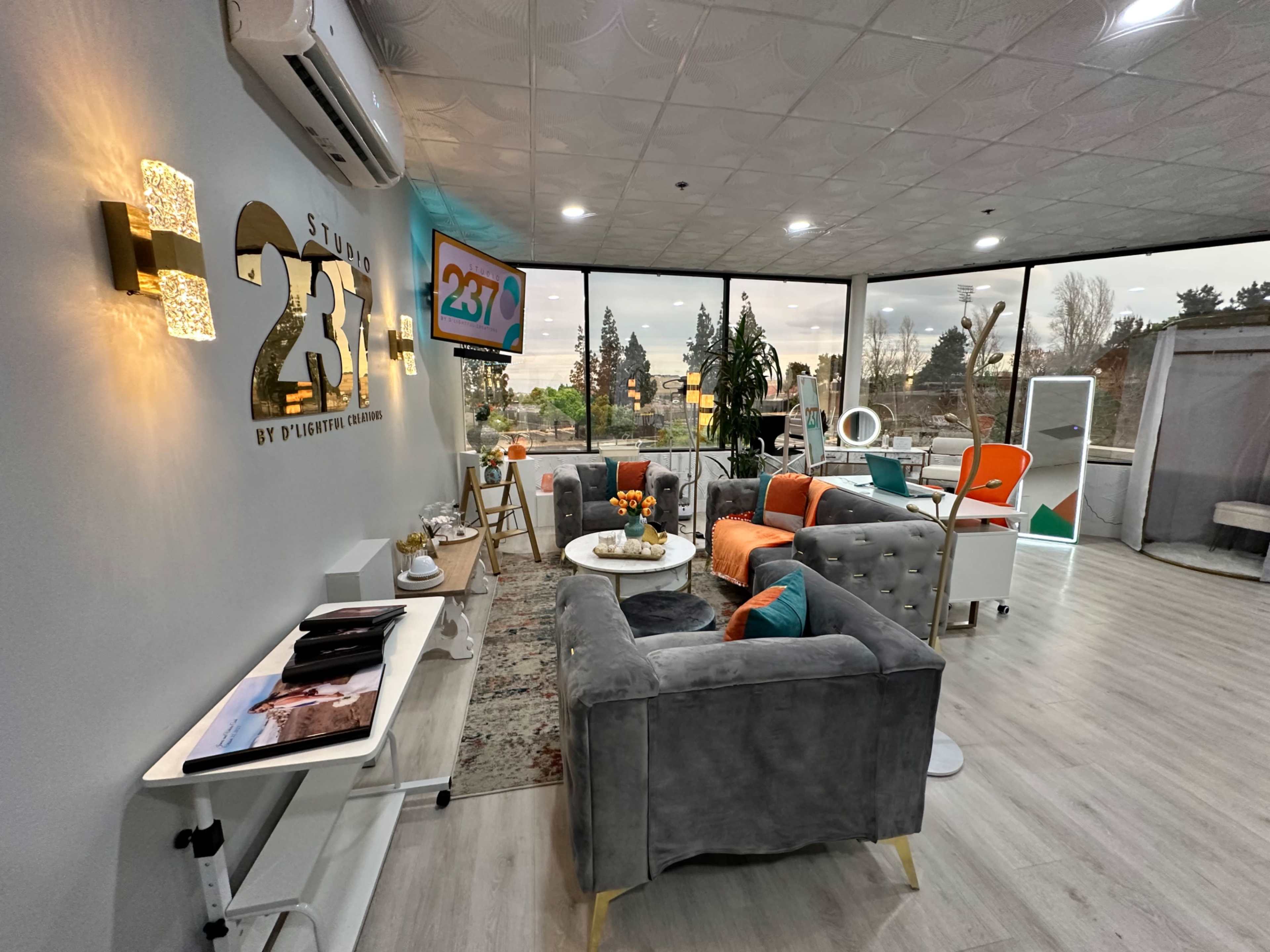 The image shows a modern, well-lit lounge area with comfortable furniture, a decorative rug, and large windows offering a view of the outdoors.