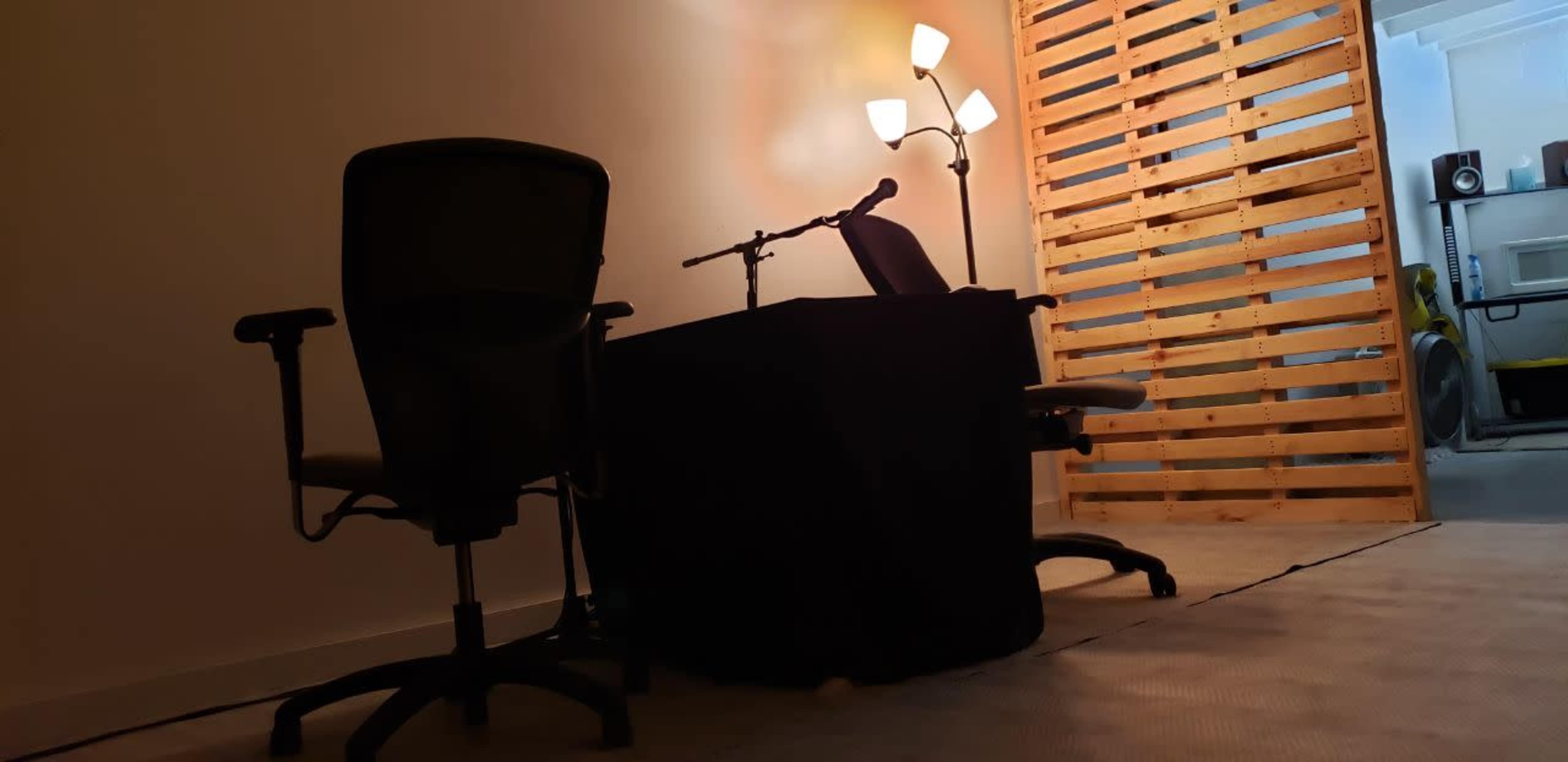 A simple workspace with two office chairs facing a small, dark table illuminated by a floor lamp, set against a wooden slatted wall.