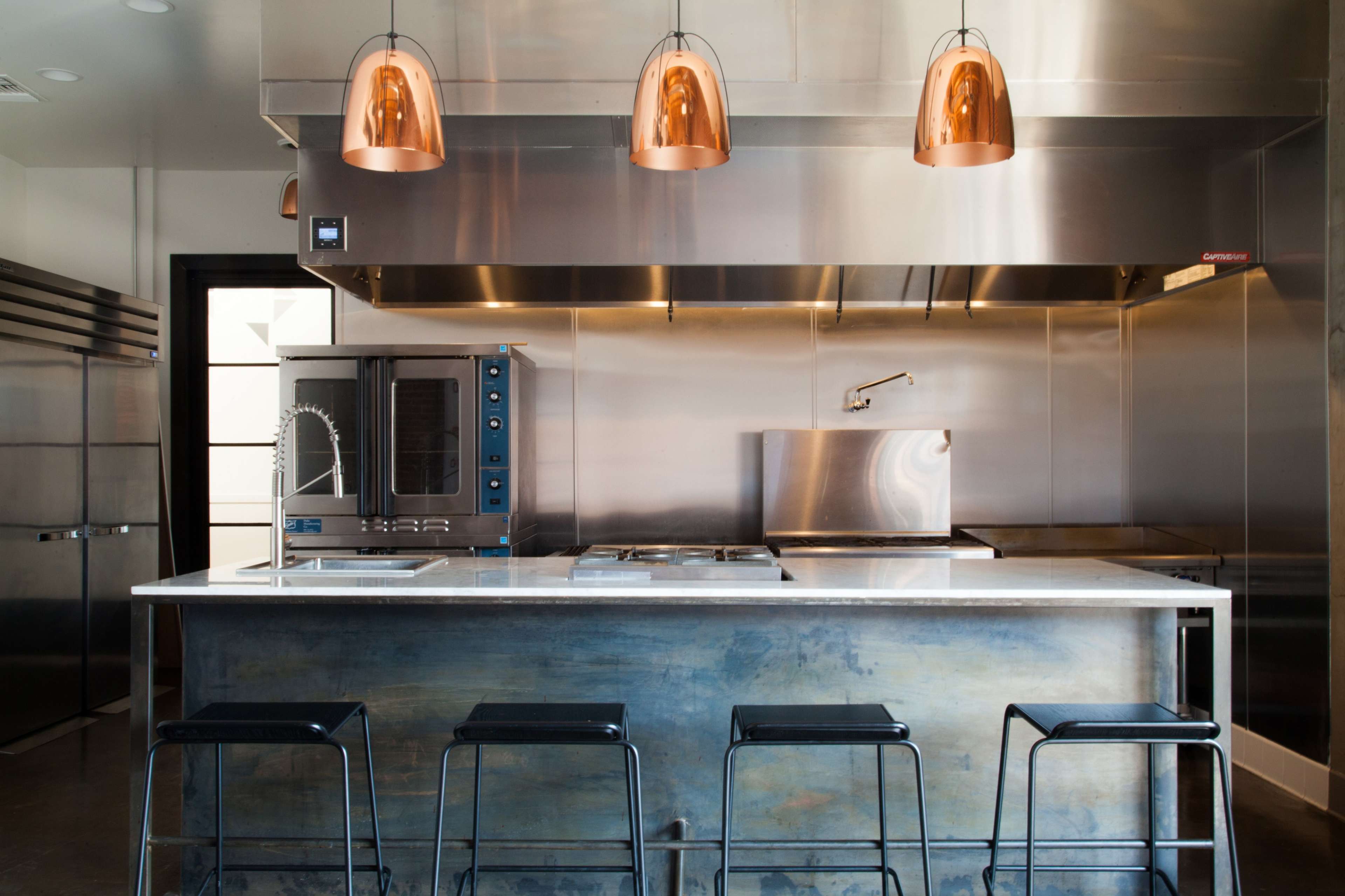 A modern kitchen with stainless steel appliances, a marble countertop, and three black stools in front of an island.