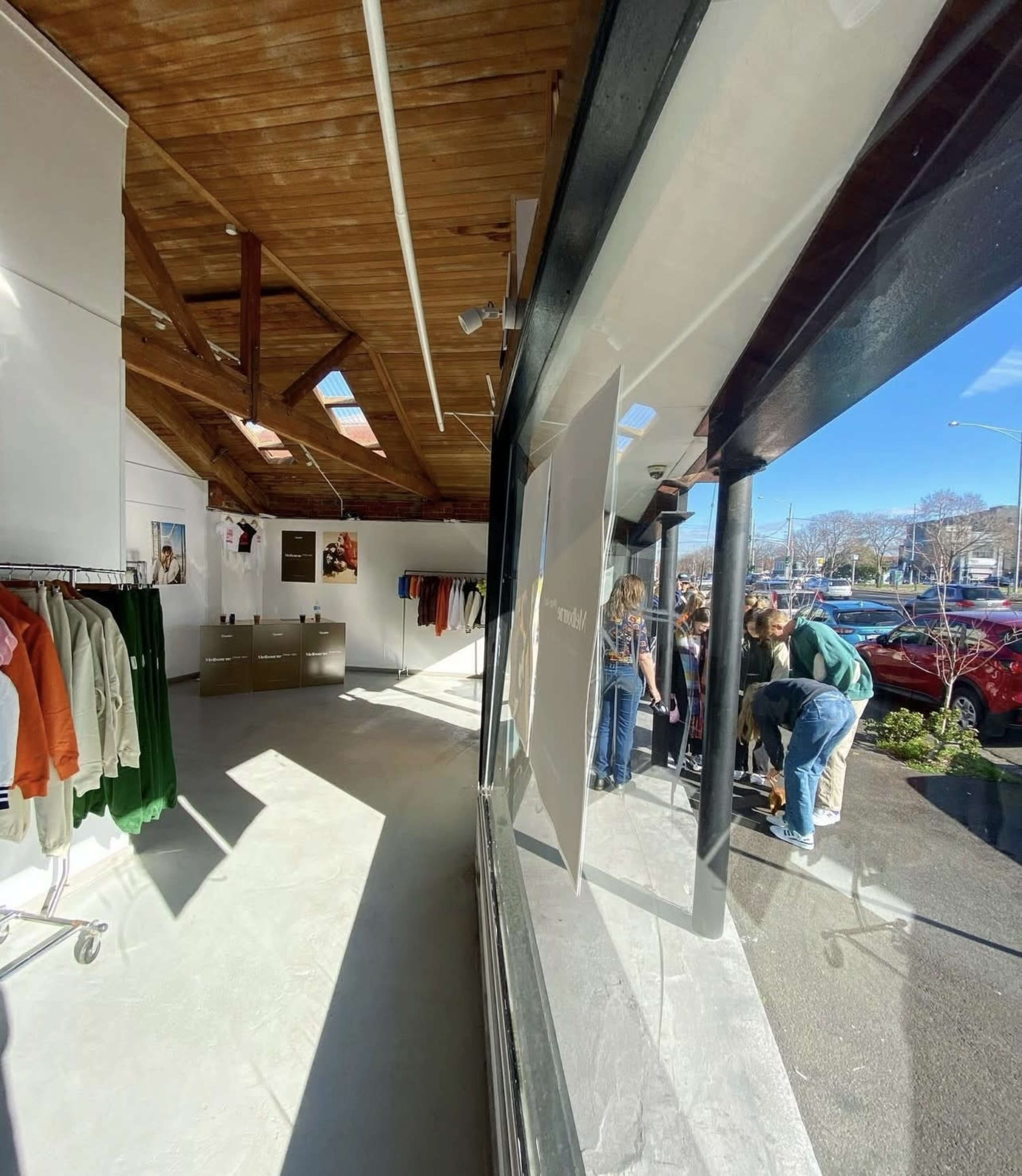 The image shows the interior of a clothing store with a wooden ceiling and display racks on one side, while a group of people can be seen outside near the entrance.