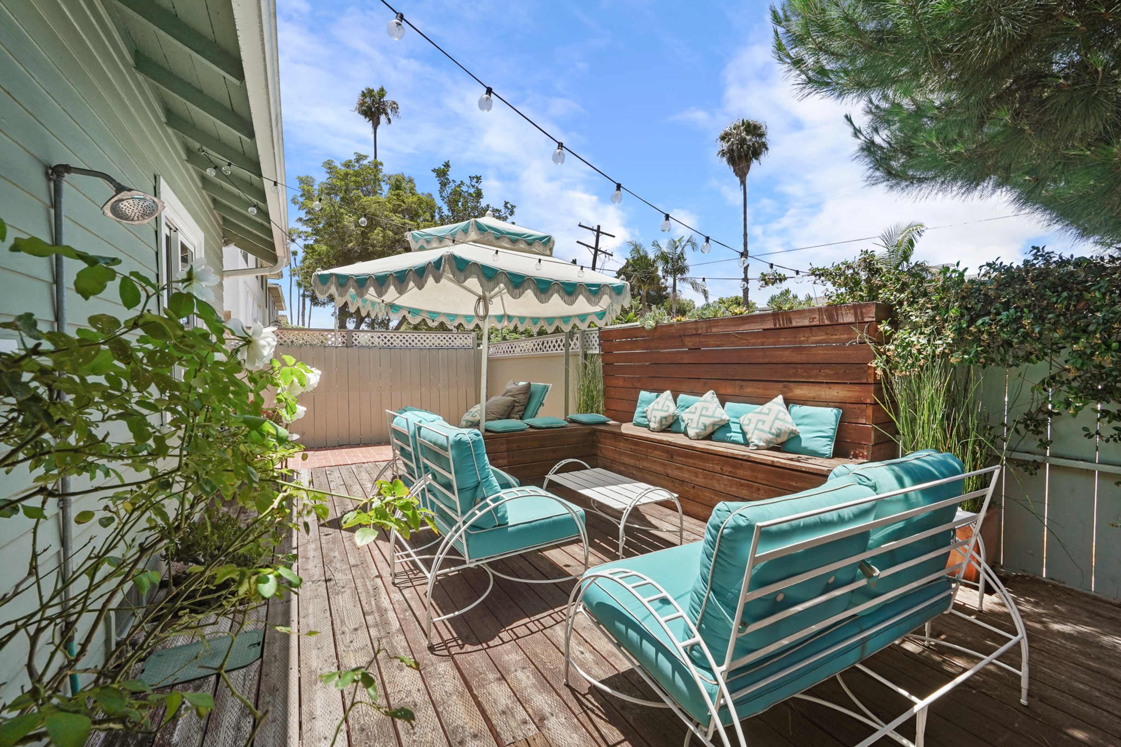 A patio area with turquoise lounge chairs, a table, and a shaded seating area surrounded by greenery and string lights.