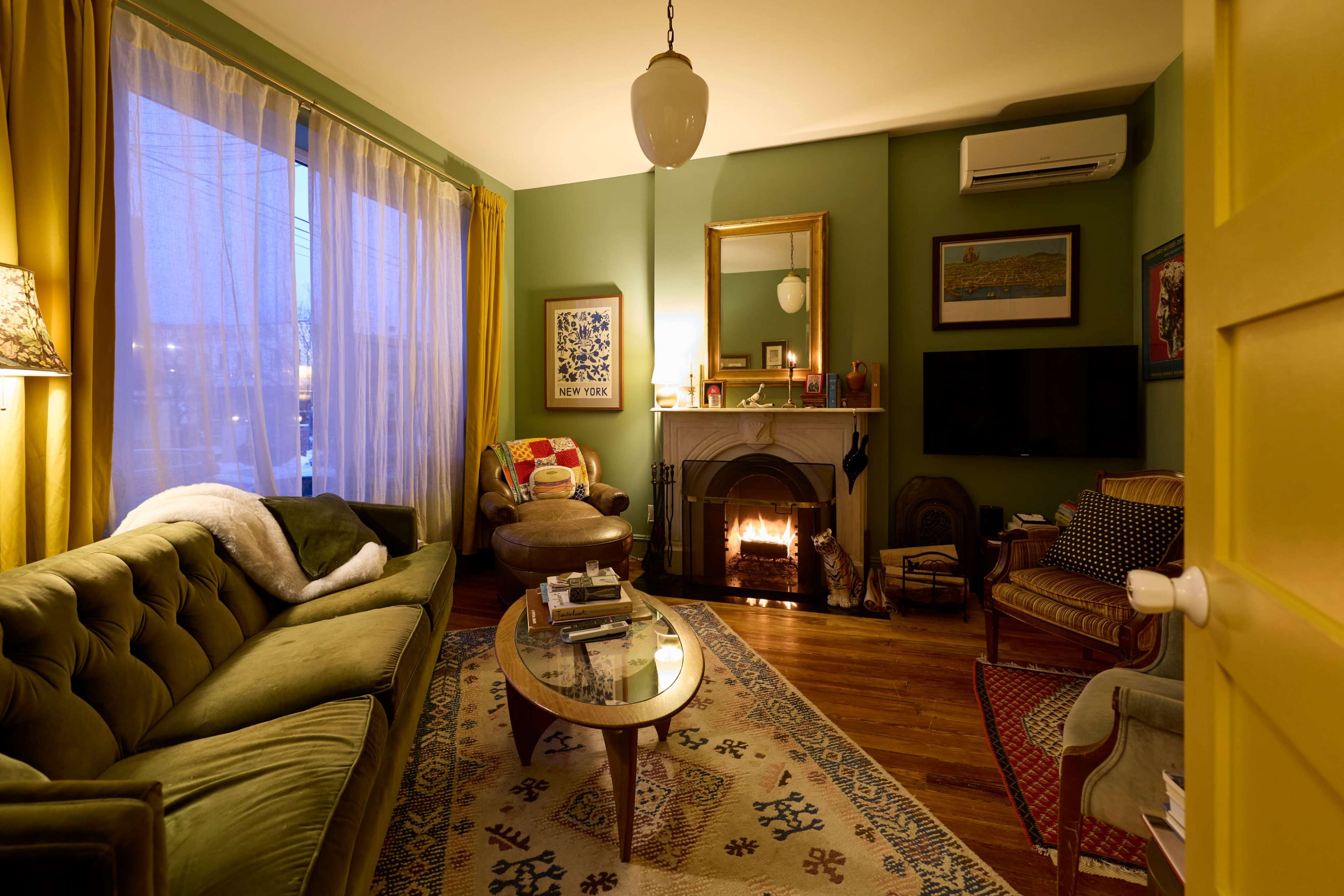 The living room features a cozy arrangement with a green sofa, a fireplace, and large windows dressed with yellow curtains.