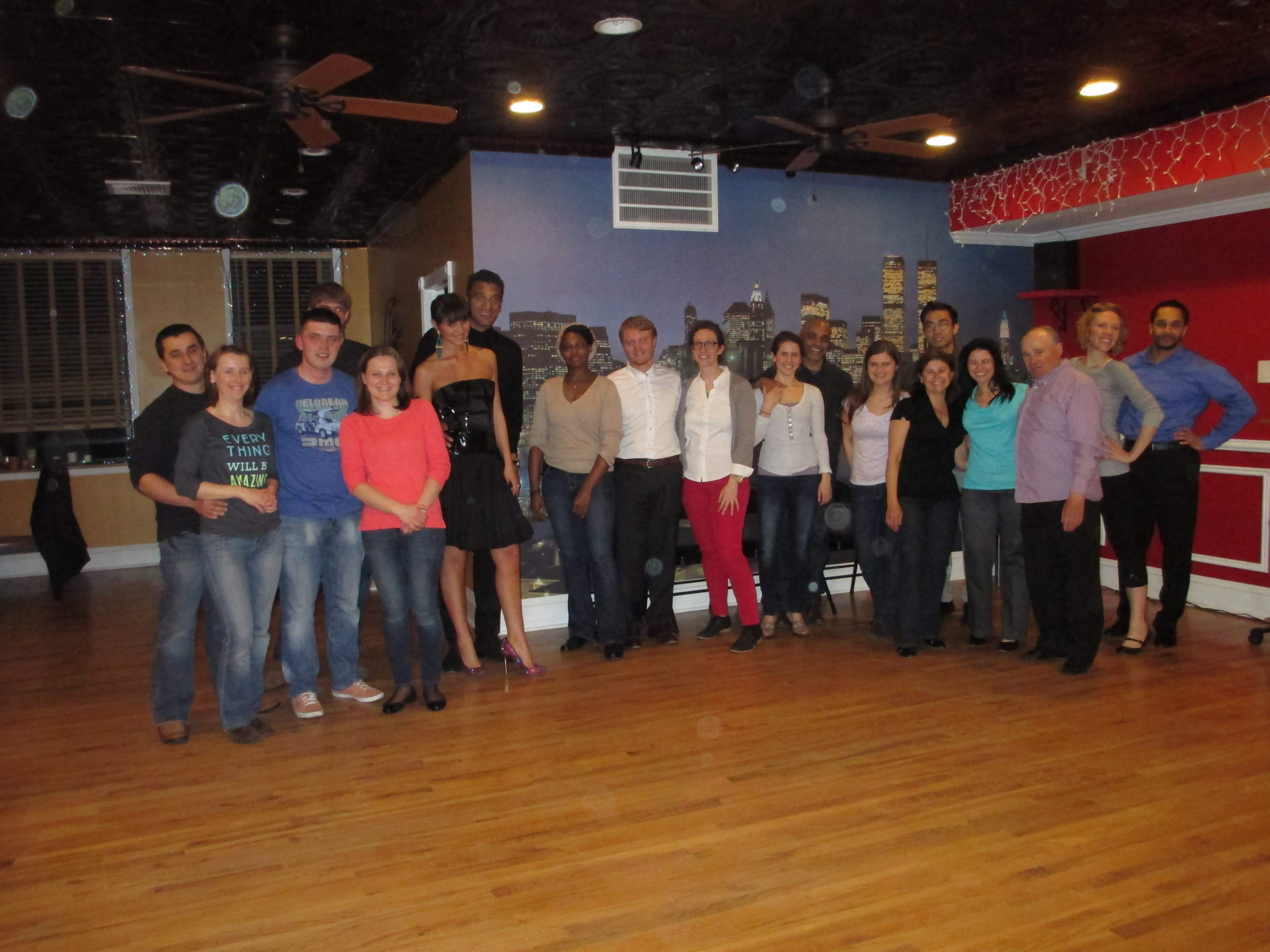 A group of people pose together in a dance studio with a cityscape mural in the background.