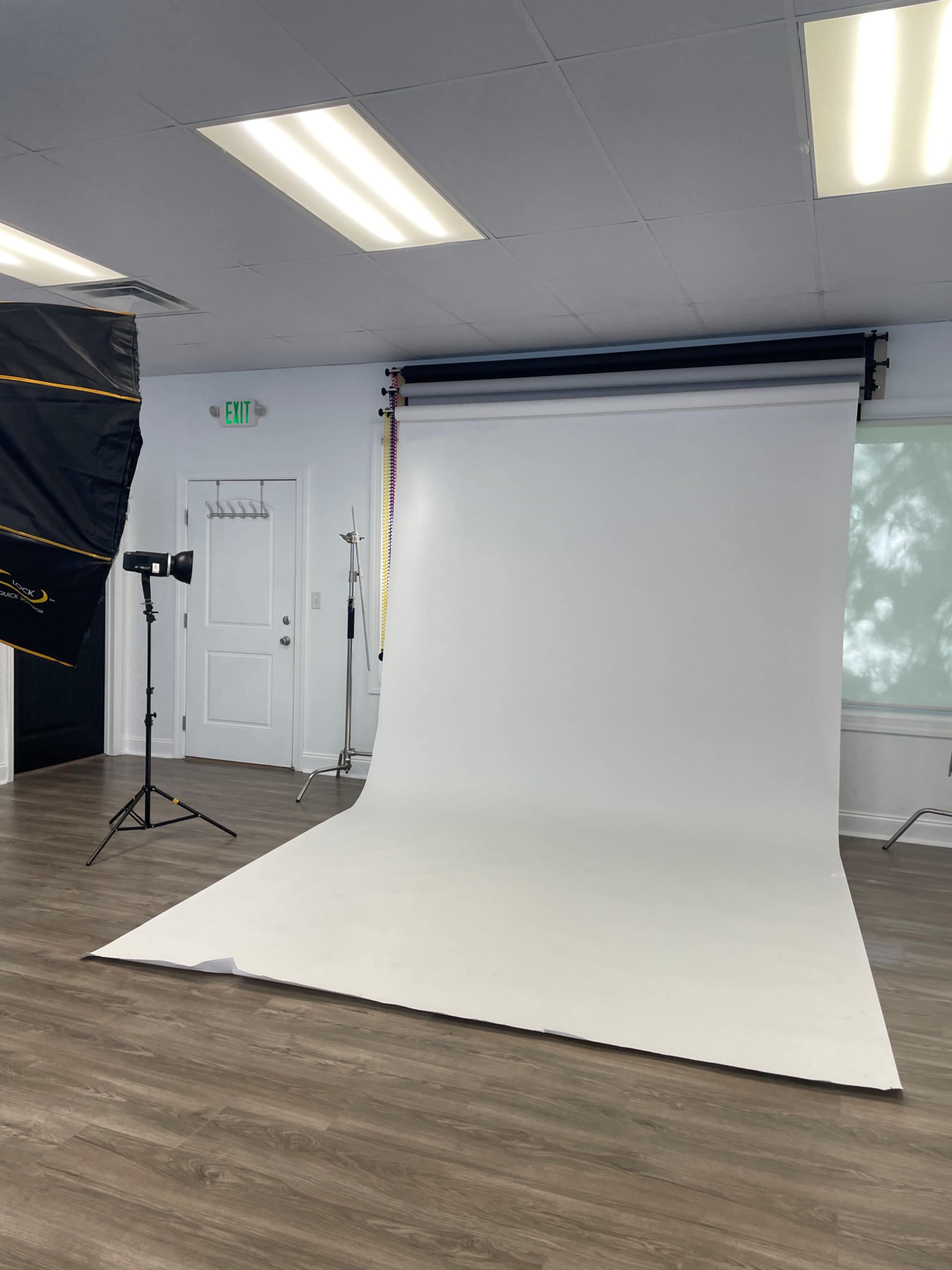 The image shows a photography studio with a white backdrop, lighting equipment, and wooden flooring.