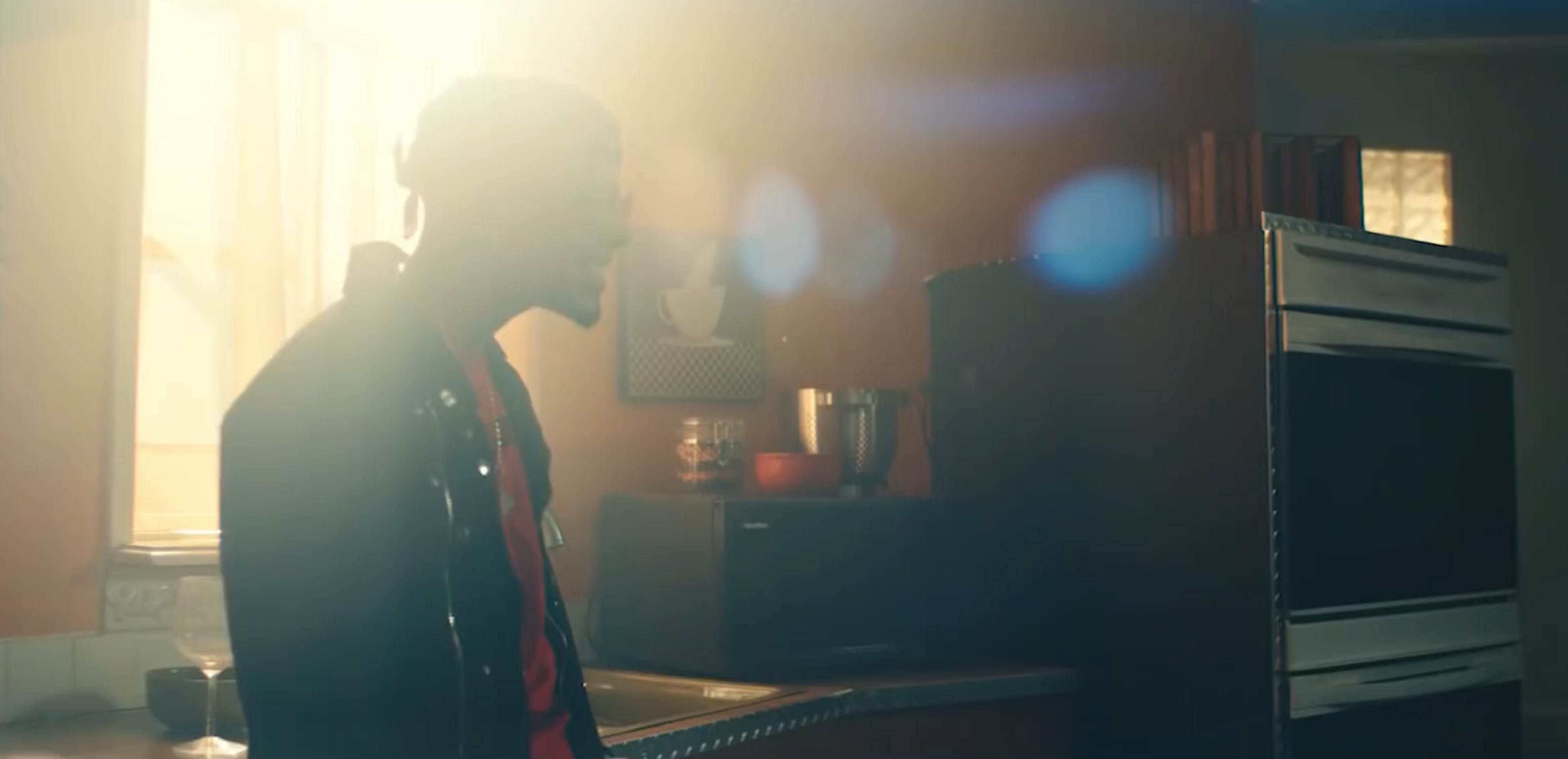 A silhouette of a person stands against a brightly lit kitchen, with sunlight streaming in through a window.