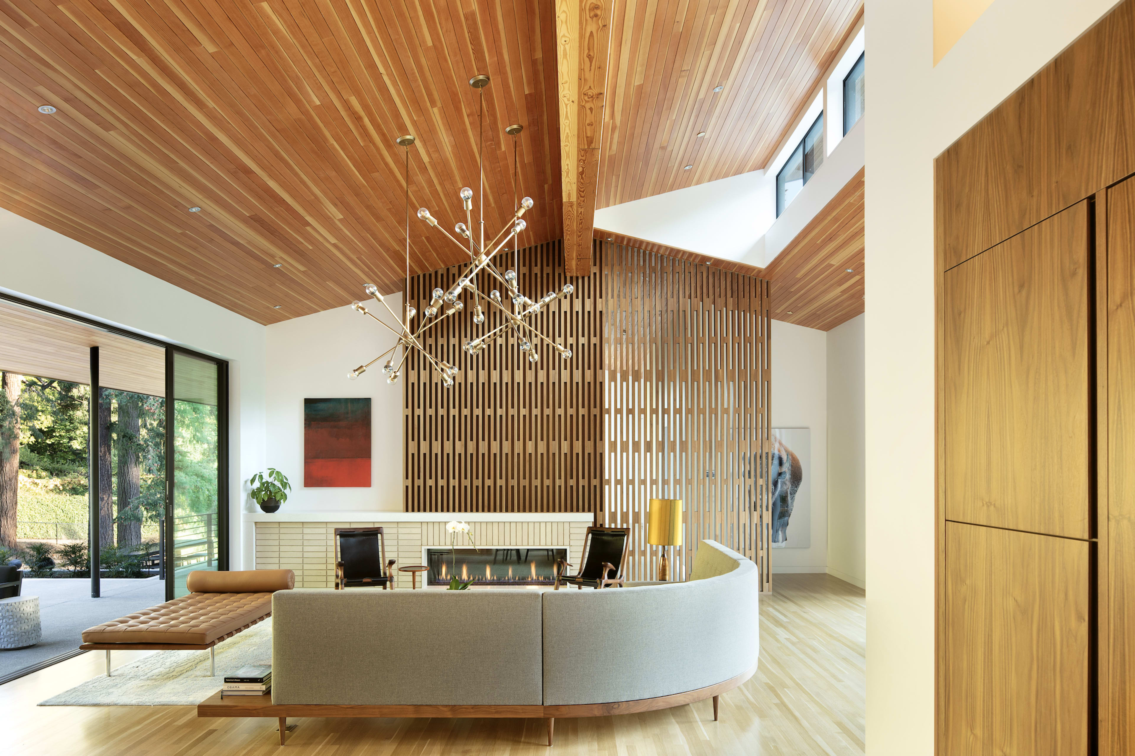 A modern living room with a curved sofa, a wooden ceiling, and large windows allowing natural light to enter the space.