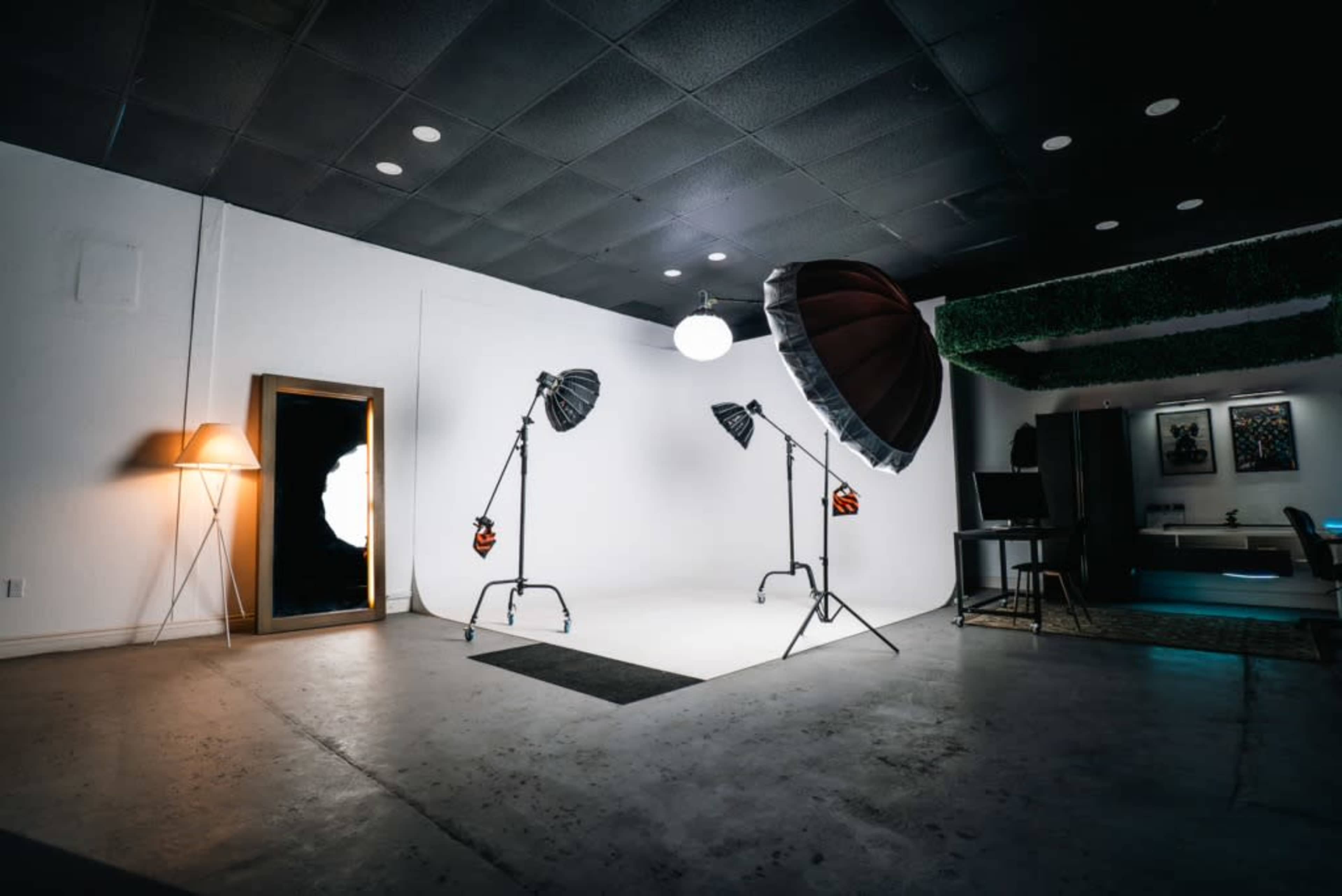 A photography studio featuring various lighting equipment, a large mirror, and a minimalist backdrop.