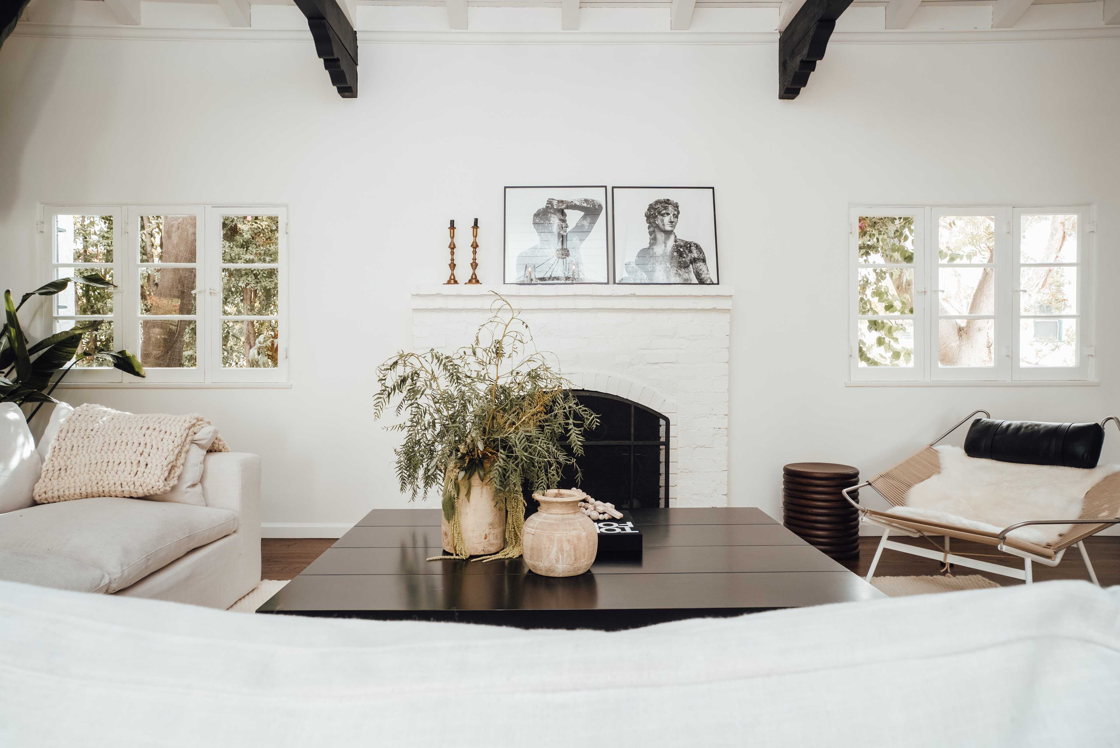 A bright living room features a white brick fireplace, two modern seating areas, and artwork on the wall.