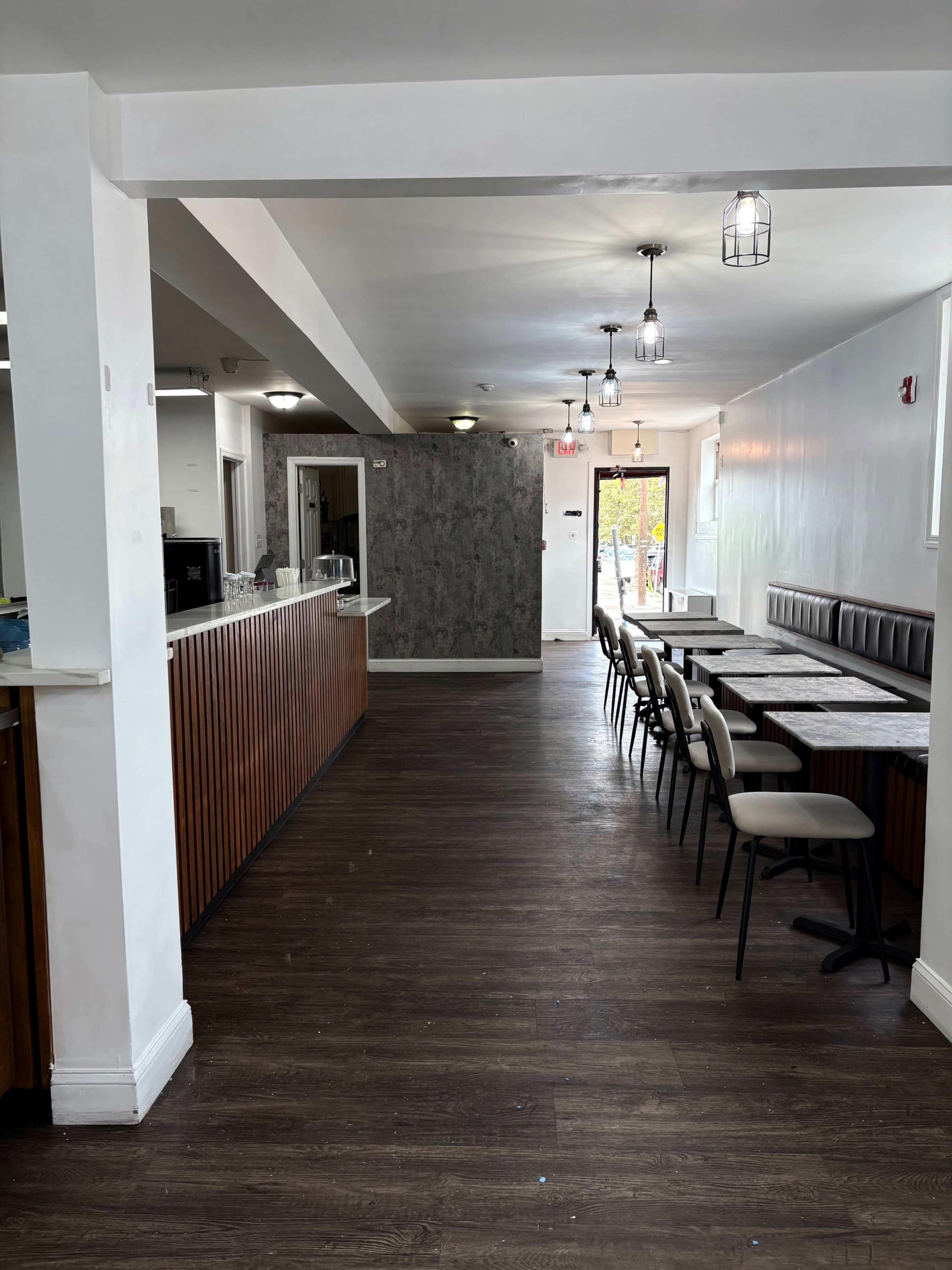 The image shows the interior of a restaurant with a long counter on one side and rows of tables and chairs arranged along the opposite wall.